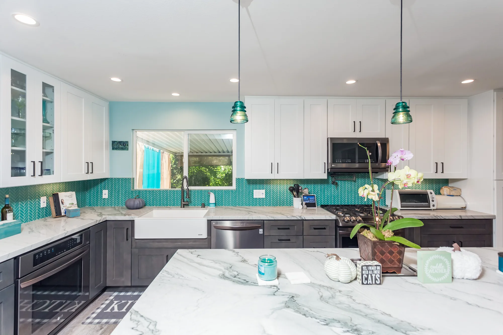 Kitchen viewed across the island toward the sink window and glass-front upper cabinets.