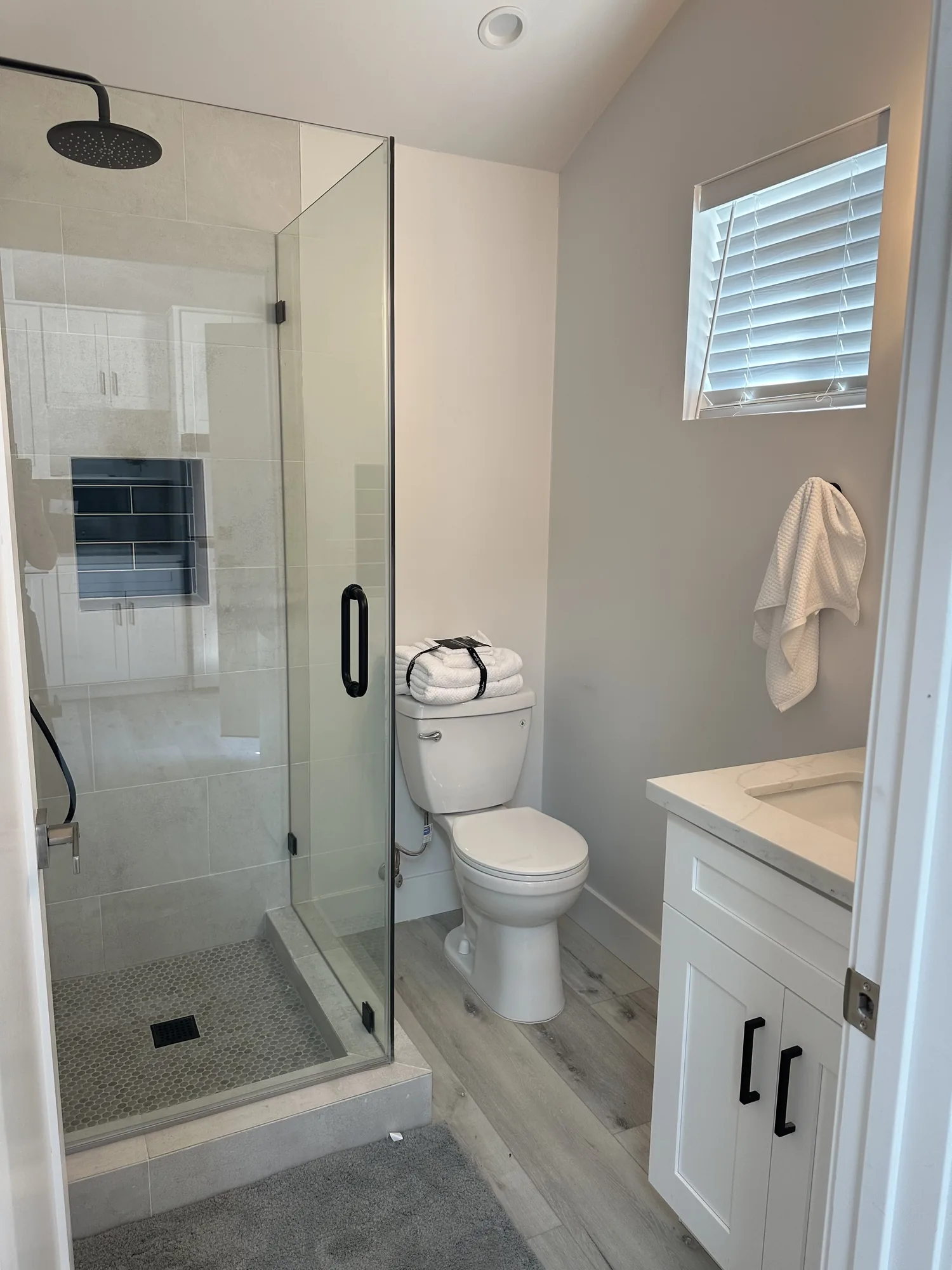 Bathroom with a corner glass shower, tiled walls, mosaic shower floor and a white shaker vanity.