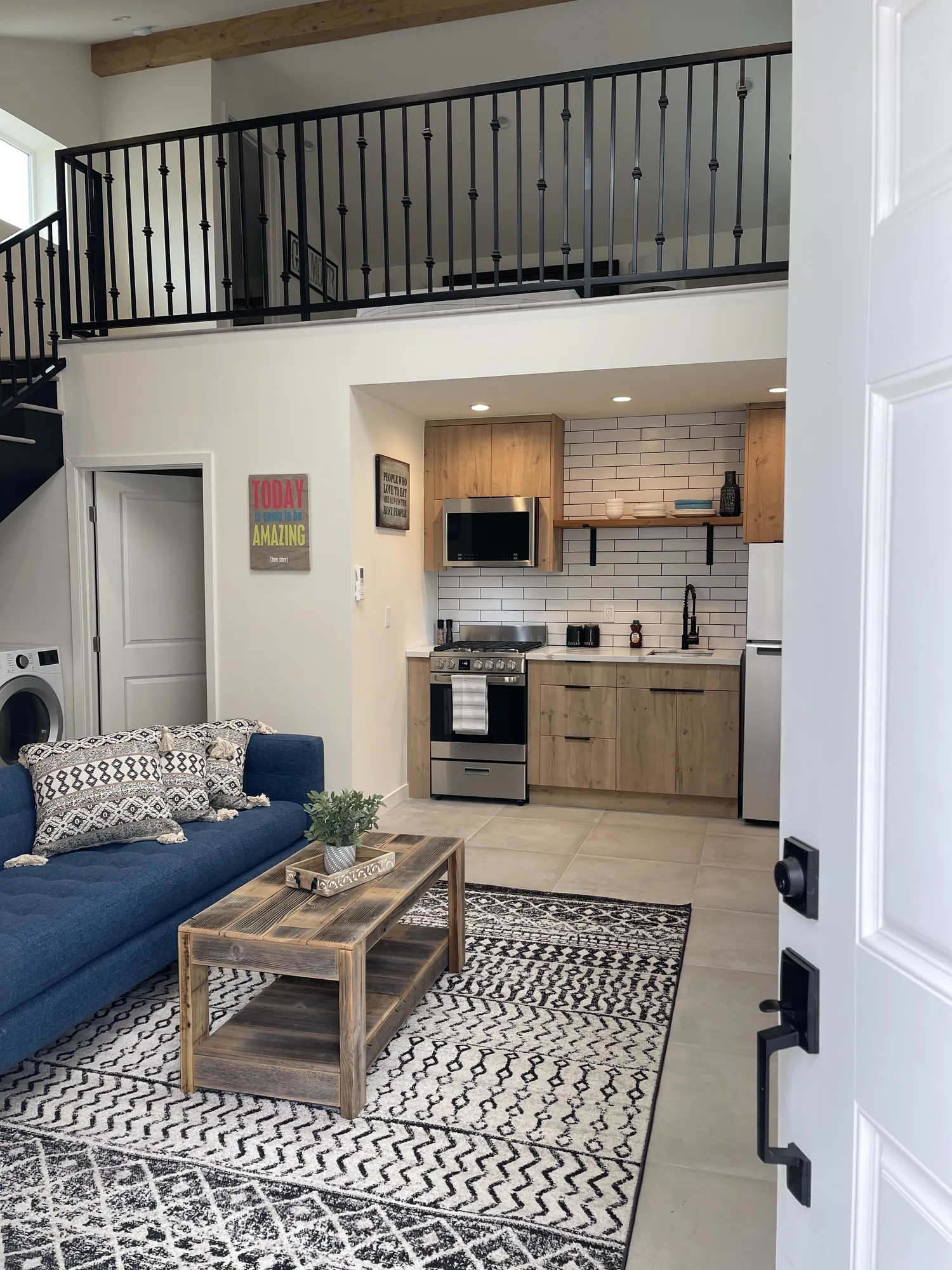 Entry view of a two-story unit showing an iron loft railing, staircase, kitchen and blue sofa.