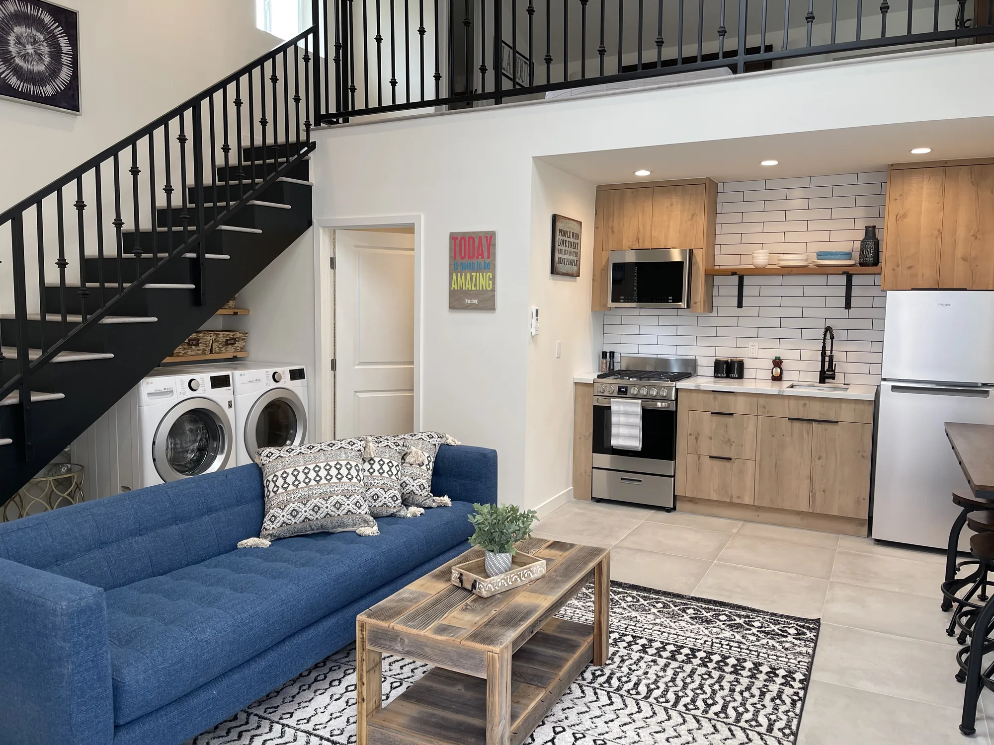 Great room with blue sofa, staircase to a loft, under-stair laundry and an open kitchen beyond.