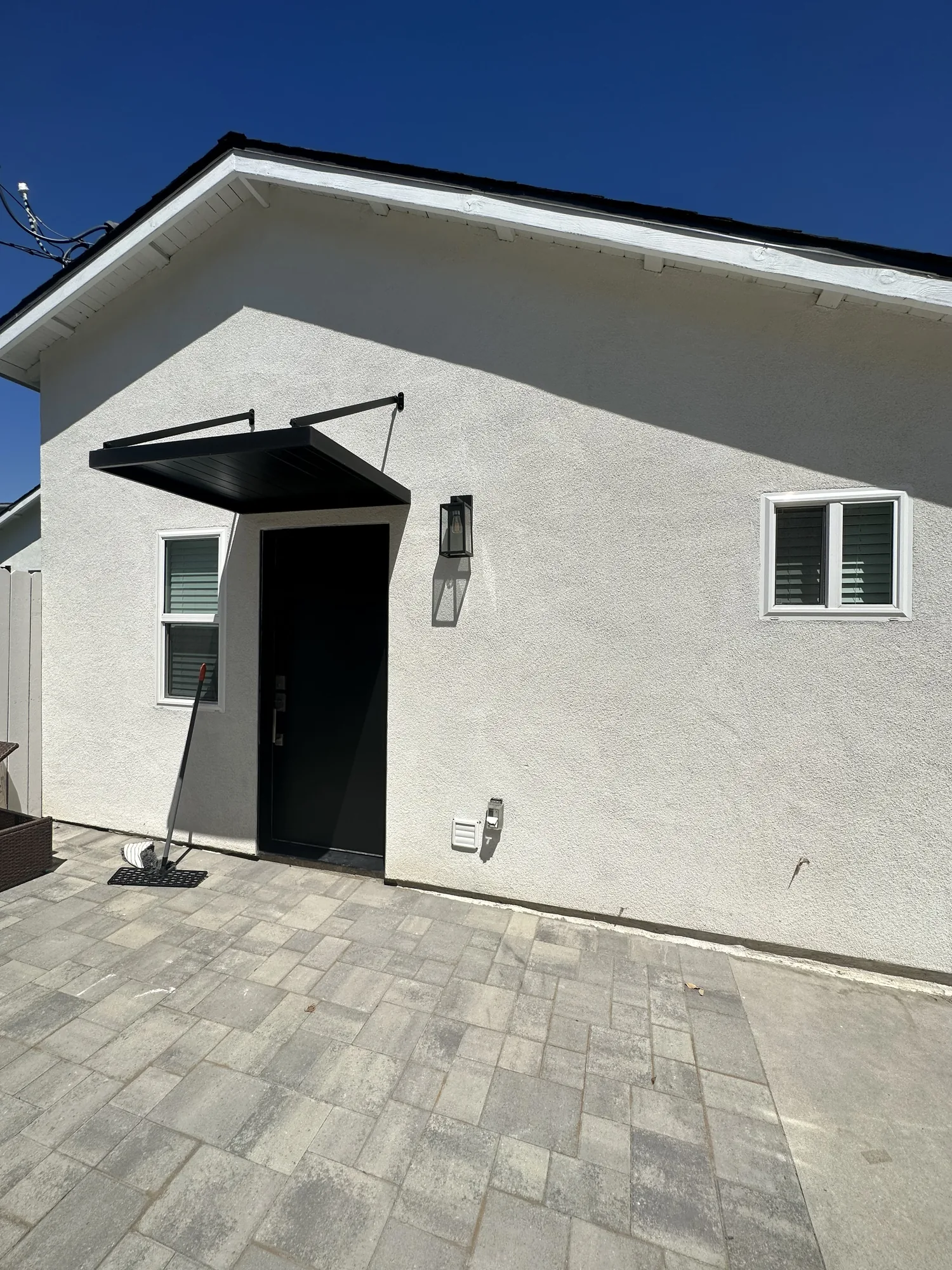 White stucco ADU exterior with a black entry door, steel awning canopy and a paver patio.
