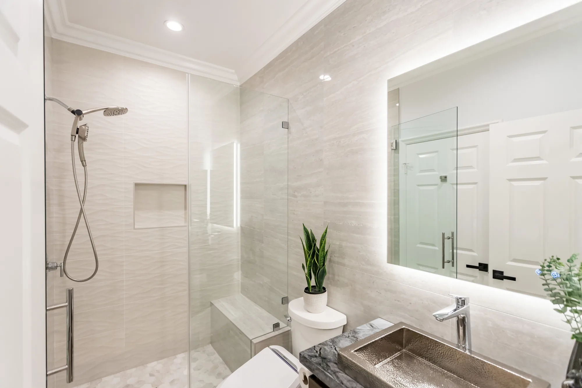 Angled bathroom view showing the tiled shower with bench seat and an LED backlit mirror above the vanity.