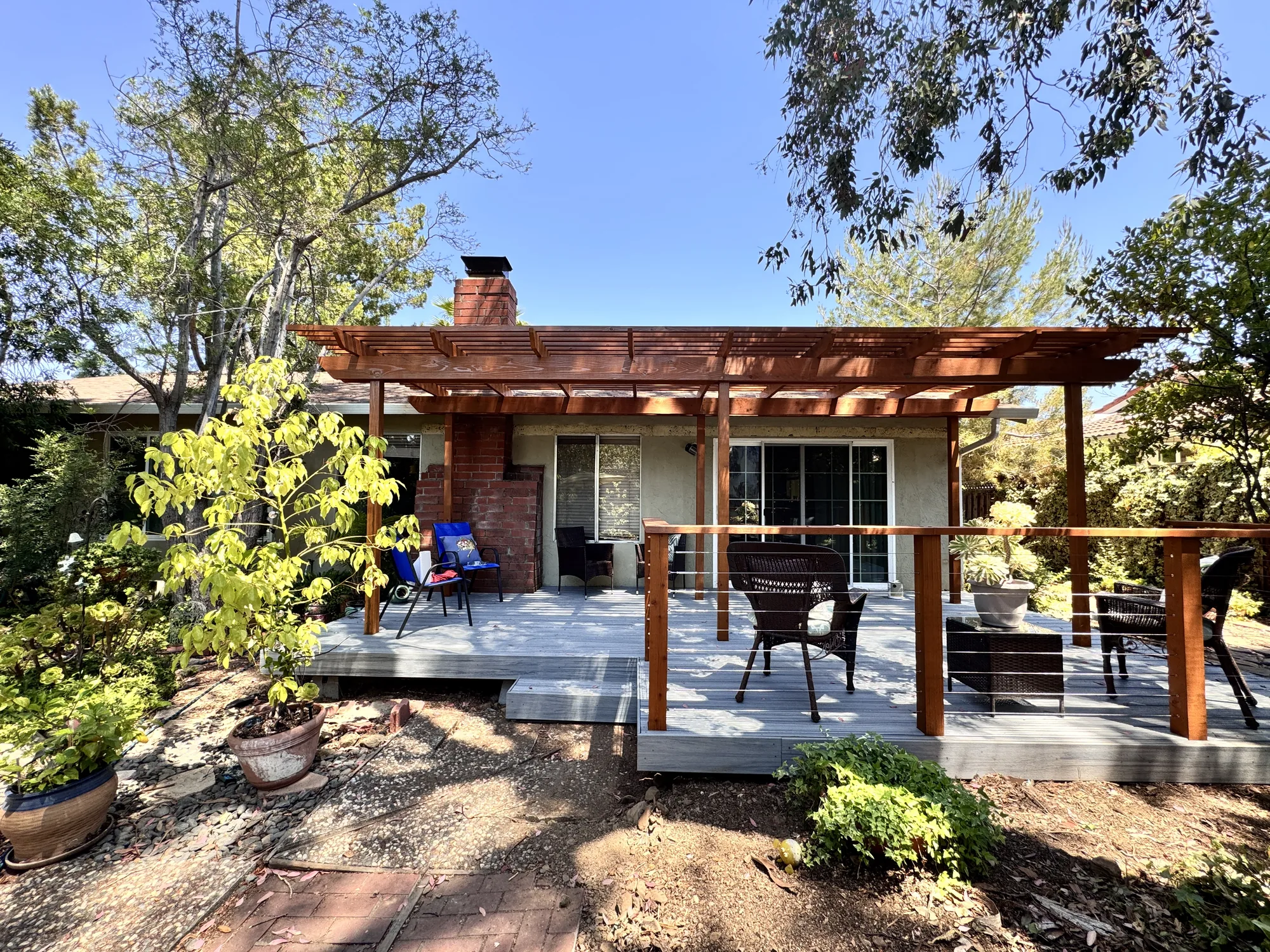 Wide backyard view of a gray deck and stained wood pergola across the back of a single-story home.