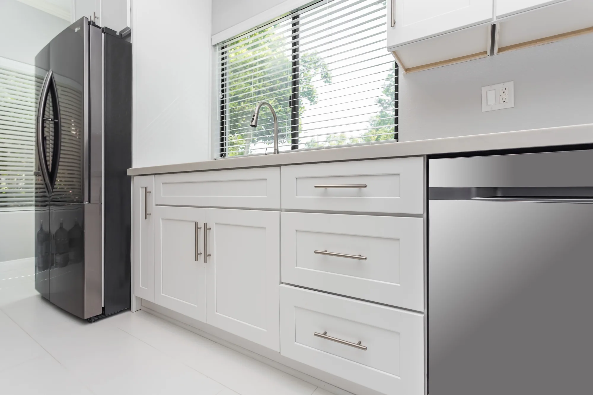 Base cabinets and a three-drawer bank in white shaker style beside a stainless dishwasher and refrigerator.