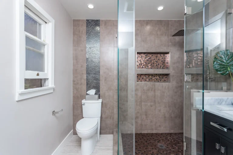 Full bathroom with glass shower, tiled toilet alcove and dark vanity beside a frosted window.
