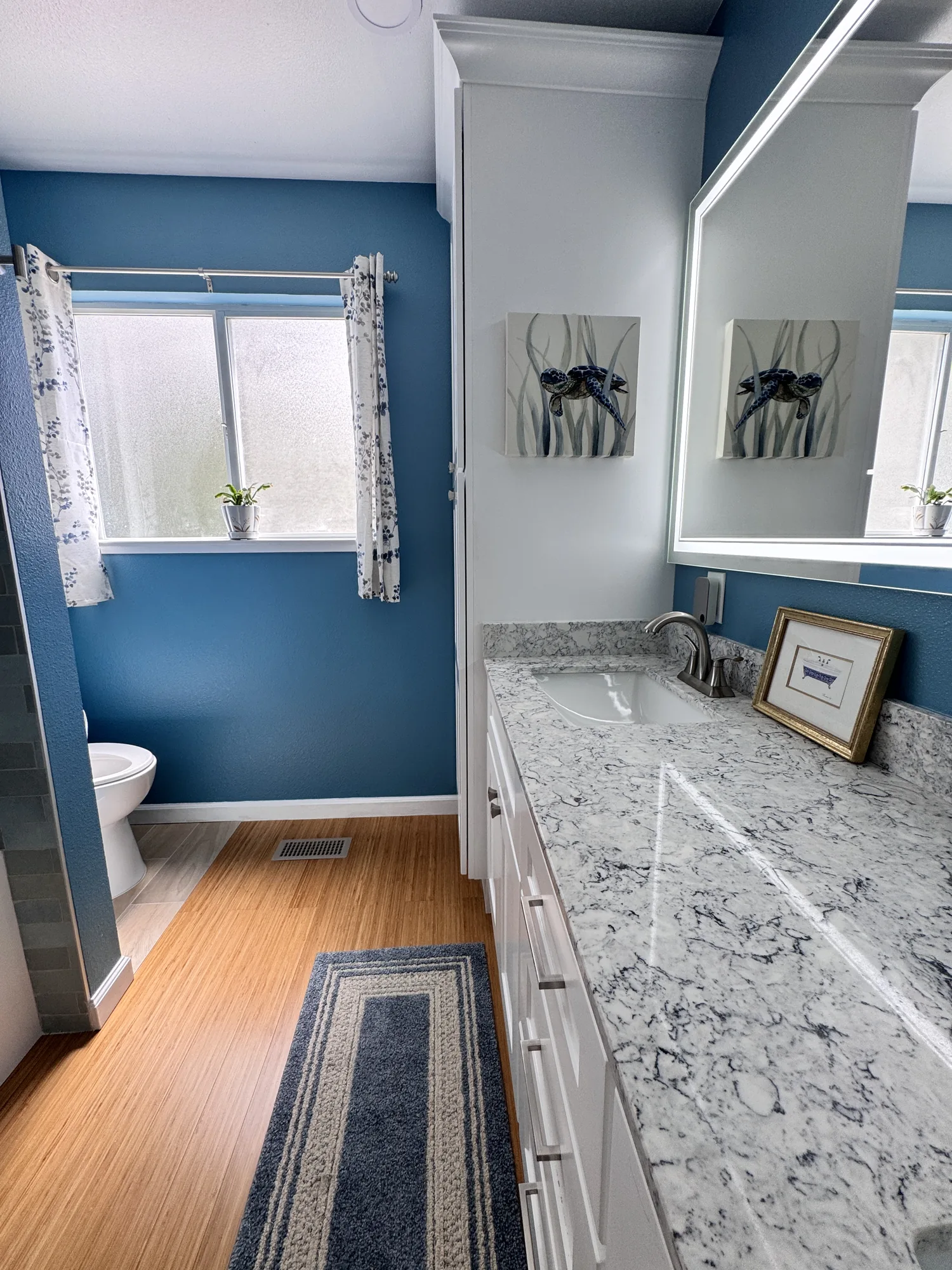 Overview of the remodeled bathroom showing the vanity, linen tower, toilet and wood-look flooring.