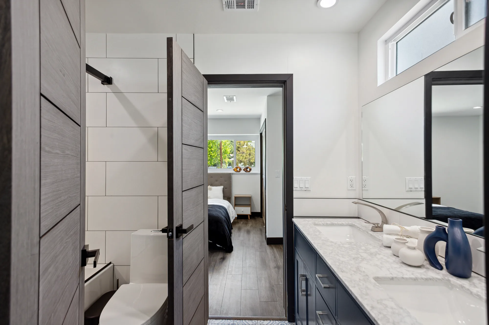 Remodeled bathroom with navy double vanity and open door looking through to the adjoining bedroom.
