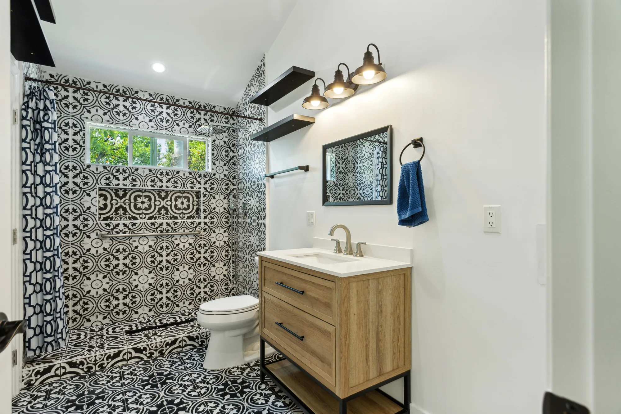 Bathroom with a curbless tiled walk-in shower, wood vanity on a black metal base, and framed mirror.