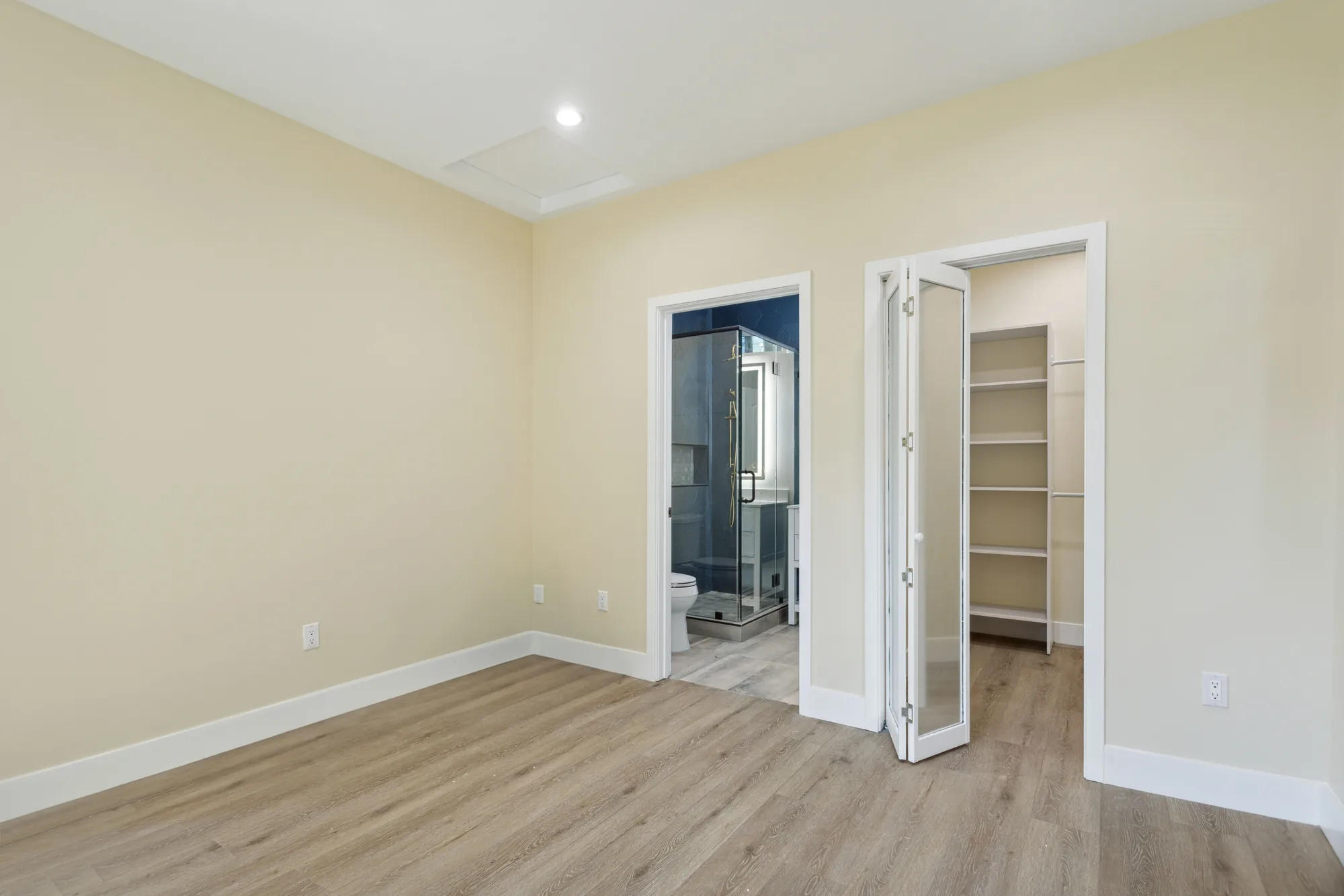 Bedroom corner with an open closet showing built-in shelving and a doorway to the tiled bathroom.