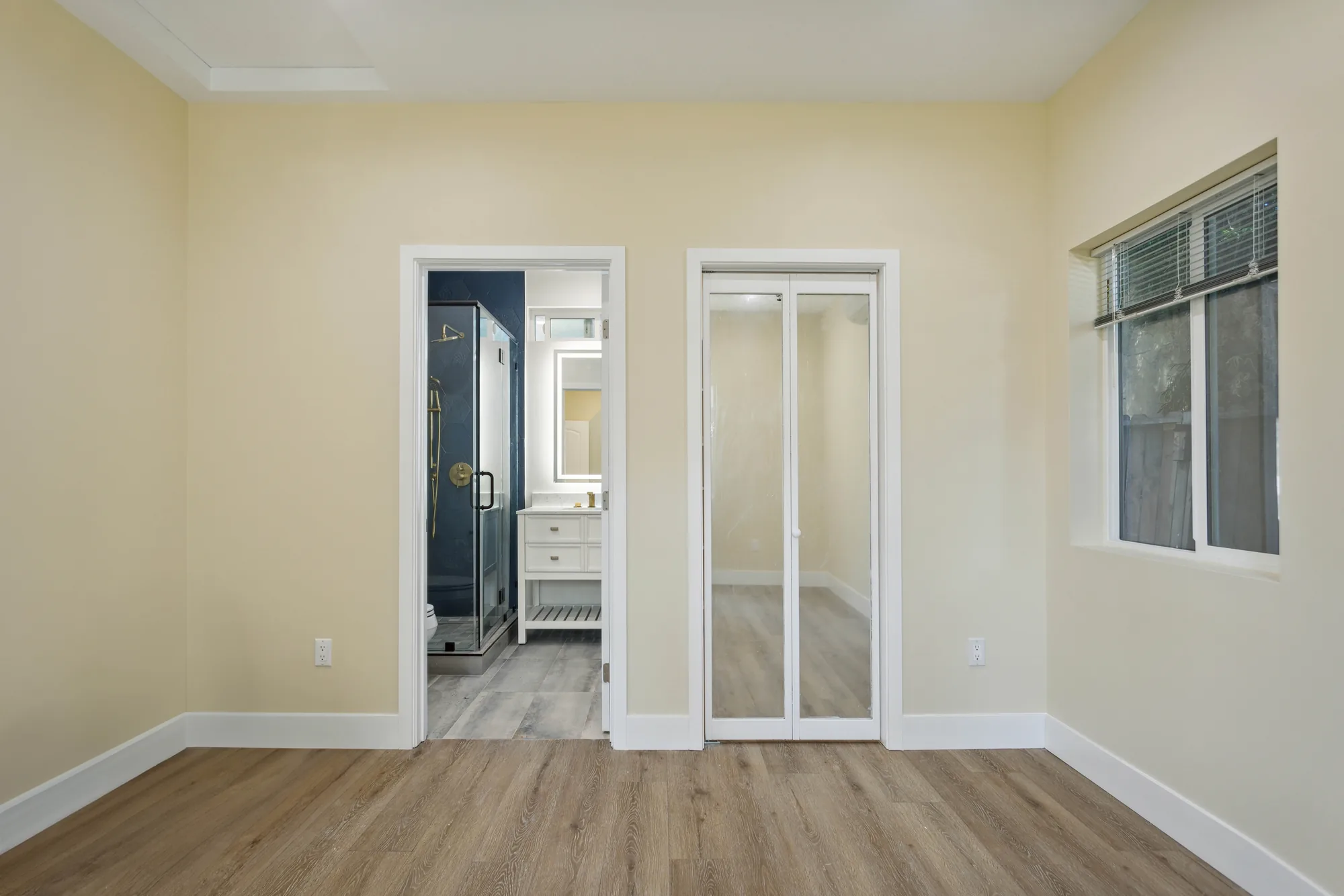 Bedroom with mirrored closet doors and a doorway showing a navy tiled shower in the ensuite.
