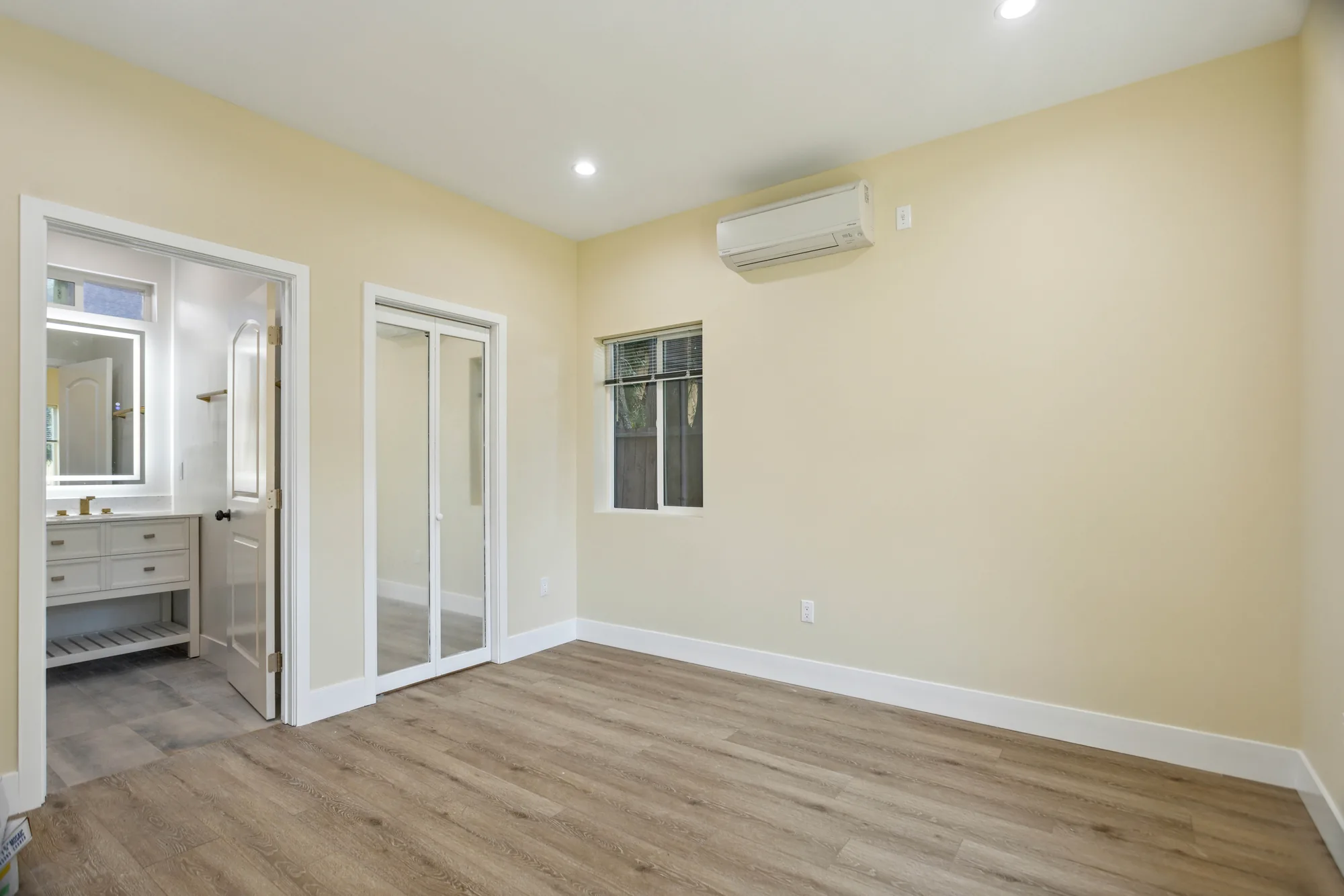 Bedroom with pale yellow walls, mirrored closet doors and an open doorway to an ensuite bath.