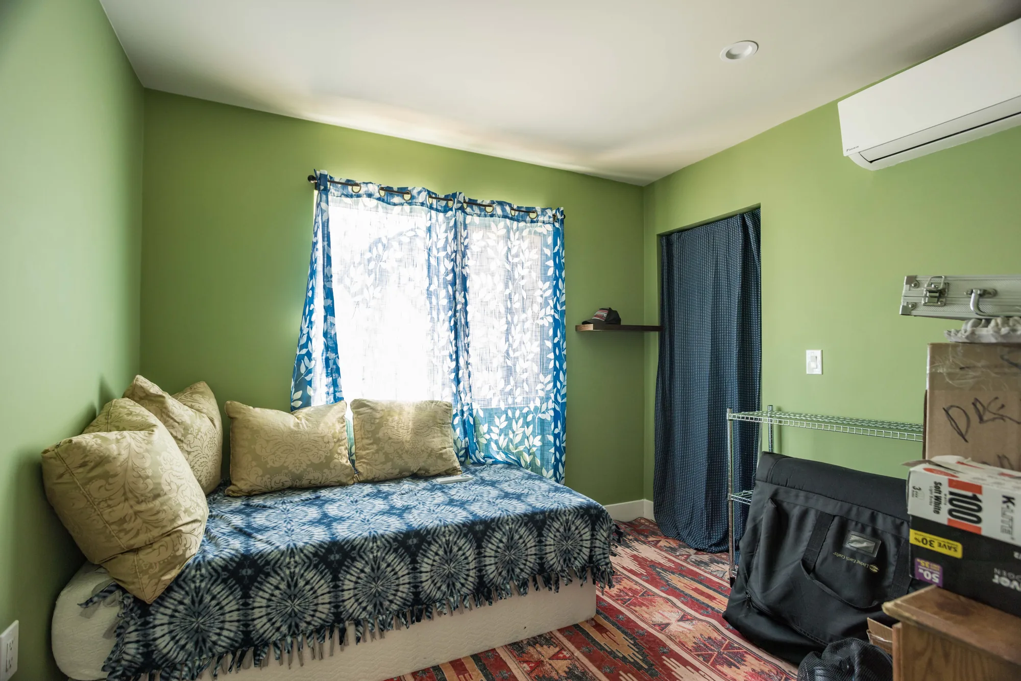 Green-walled bedroom with a curtained window, daybed, and a wall-mounted mini-split unit above.