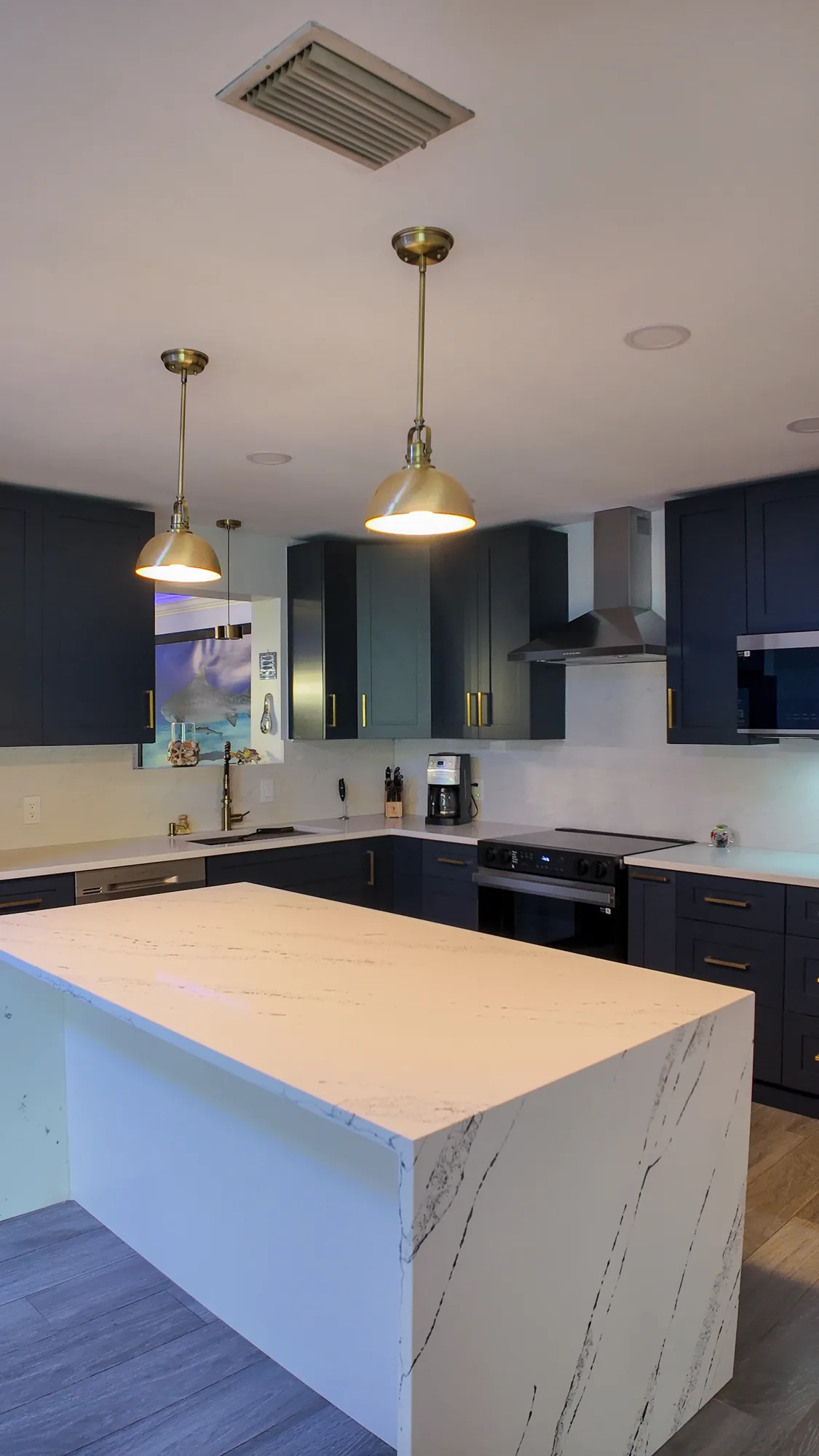 Two brass dome pendant lights hang above a white quartz kitchen island with navy cabinets behind.