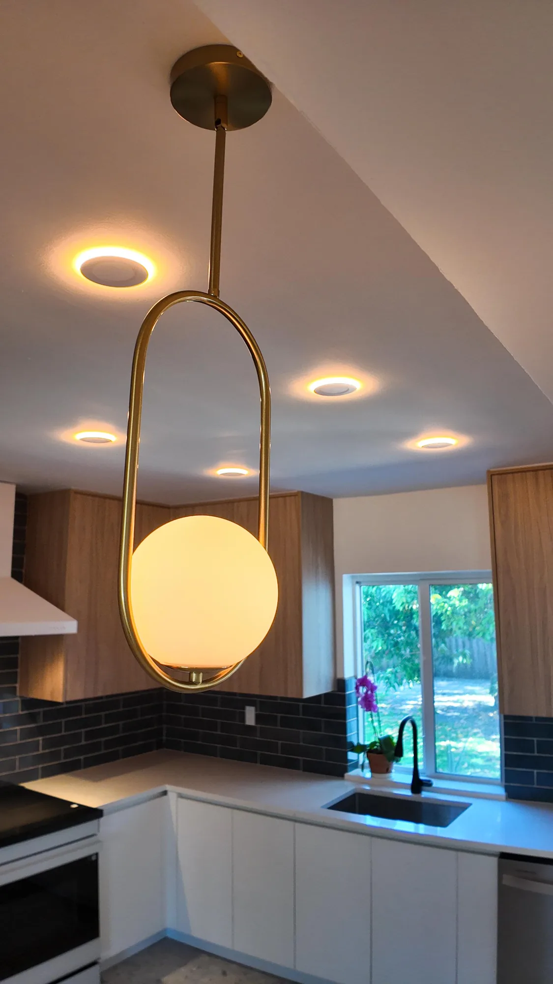 Brass ring pendant with a round glass globe hanging above a light quartz counter in a modern kitchen.