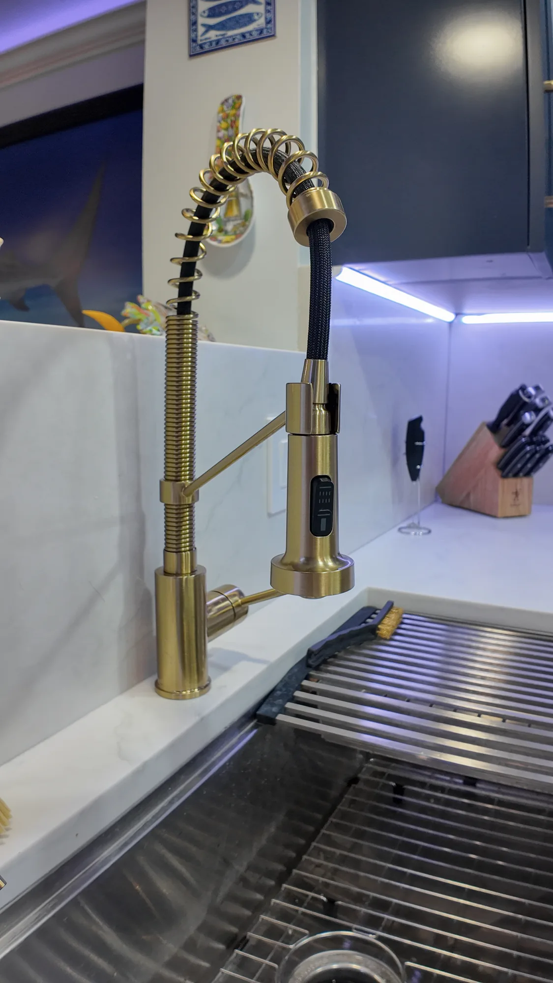 Brass spring-coil pull-down kitchen faucet at a stainless sink with a quartz backsplash behind it.