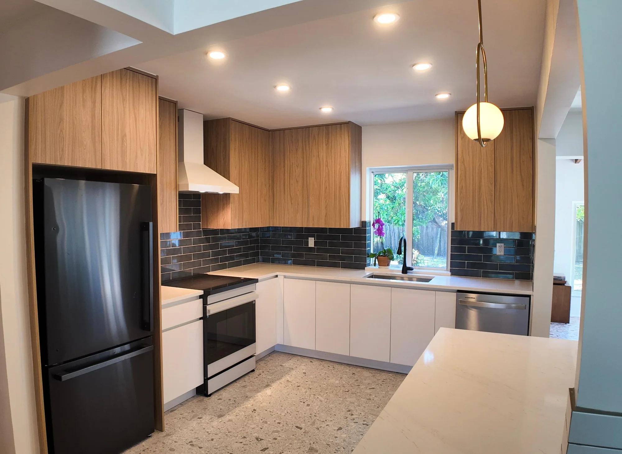 Bright modern kitchen with wood and white cabinets, dark tile backsplash and a garden window over the sink.