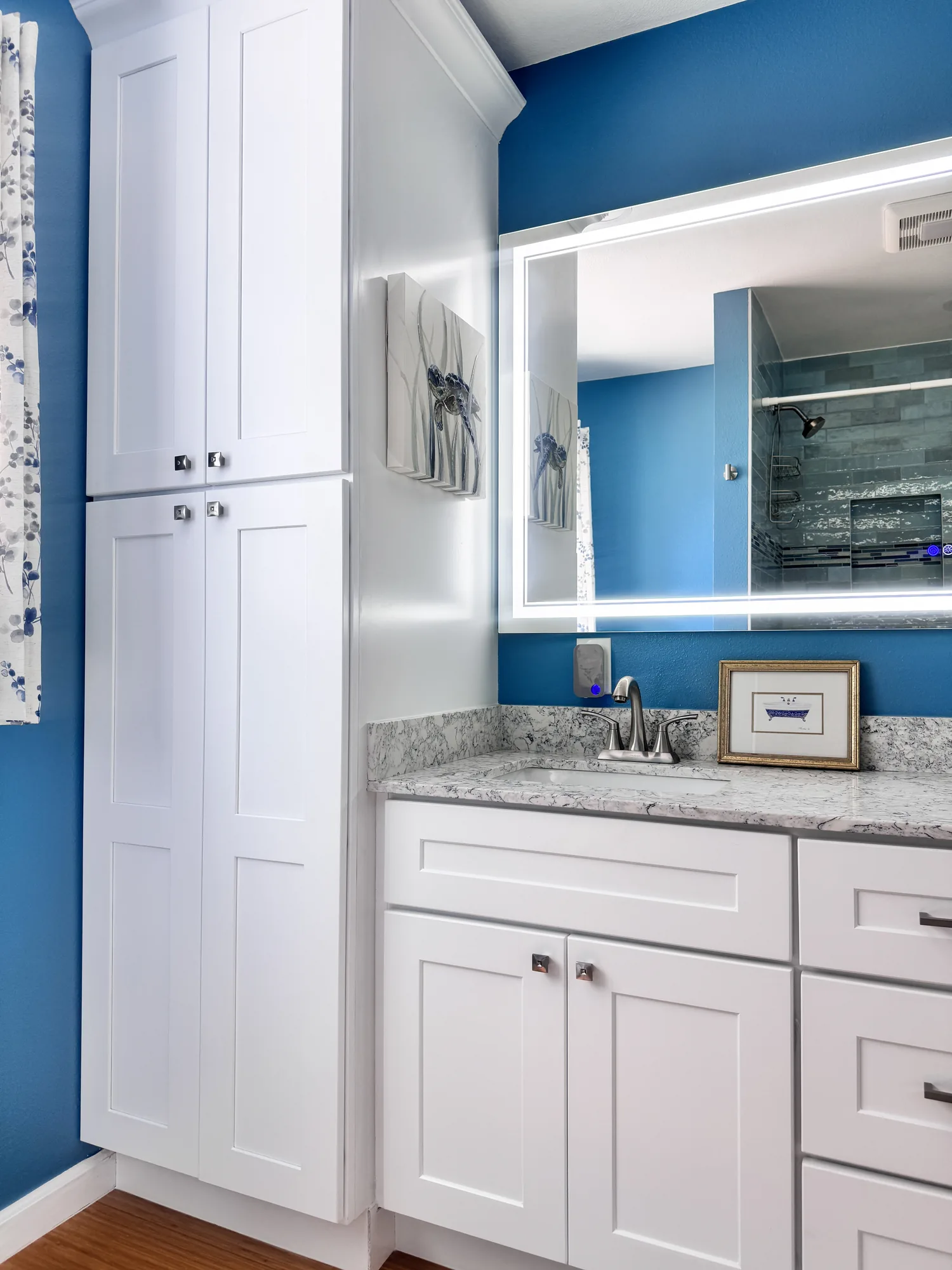 Floor-to-ceiling white shaker linen cabinet built in beside the vanity against a deep blue wall.