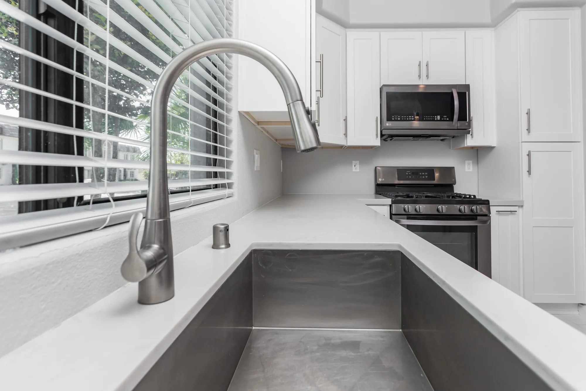 View along a light countertop from the undermount sink toward a stainless gas range and microwave.