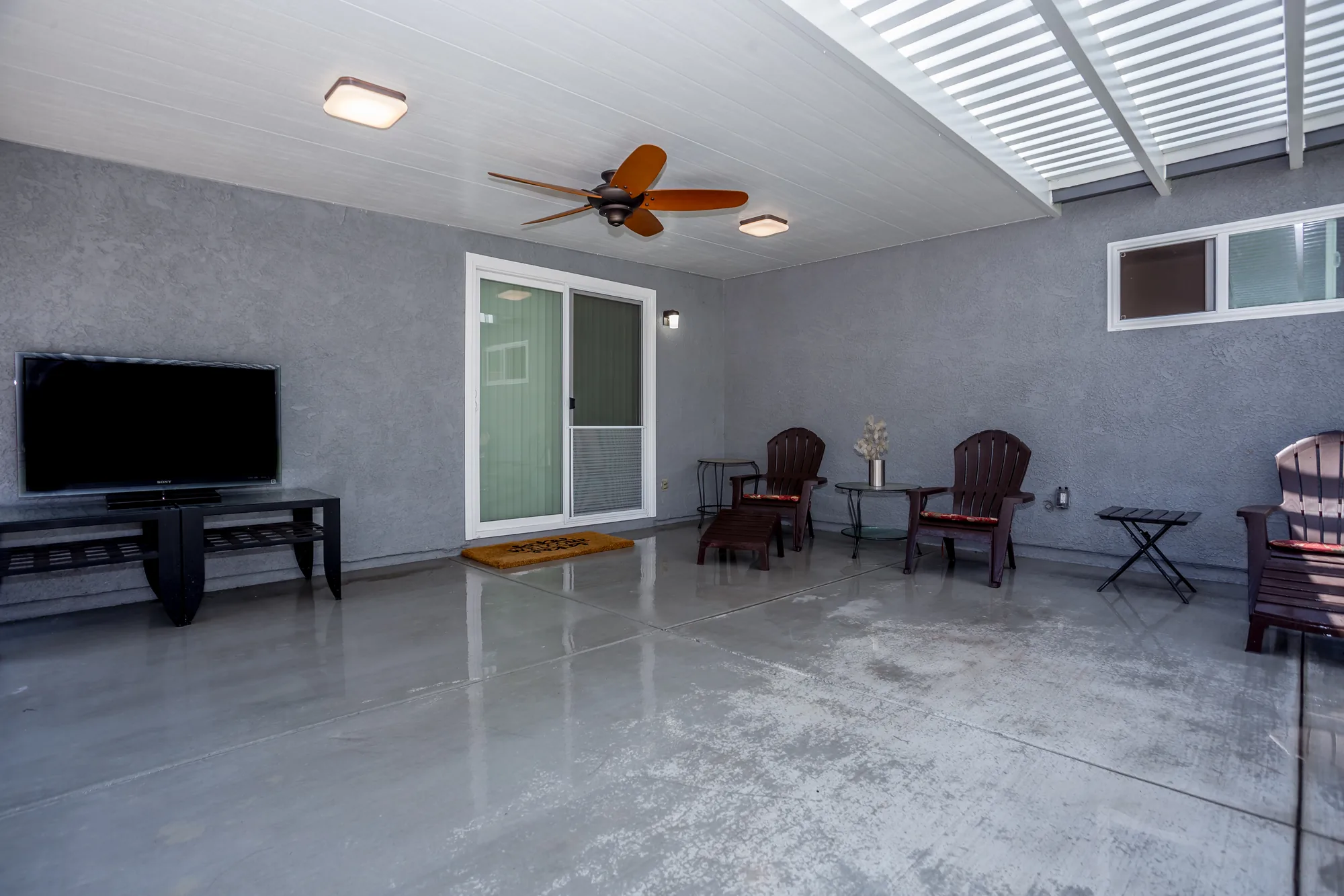 Covered patio seating area with a white plank ceiling, ceiling fan and sliding glass door to the house.