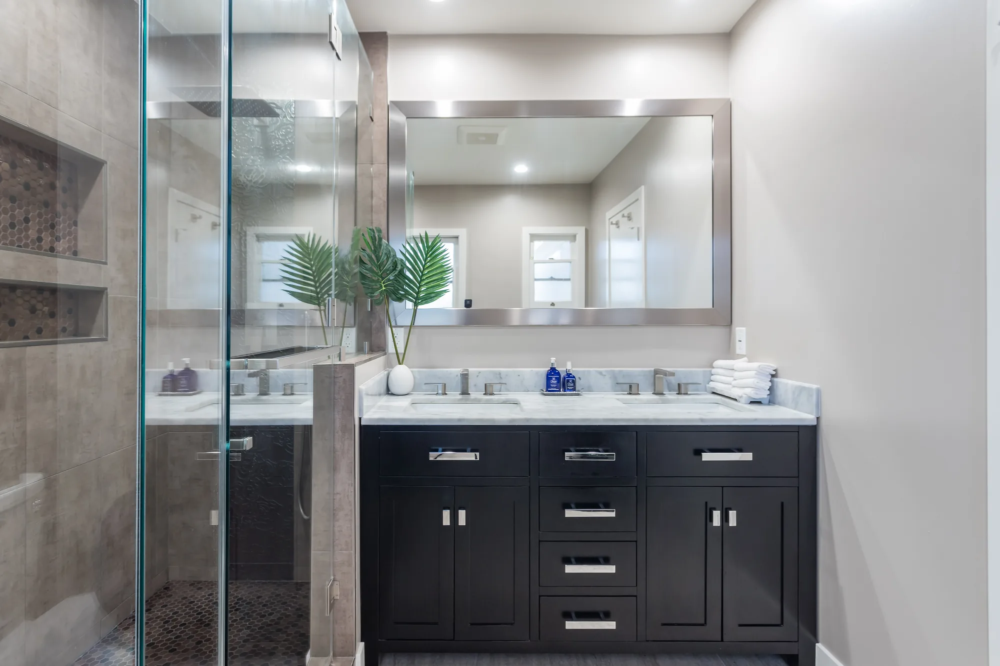 Dark shaker double vanity with a marble-look counter and framed mirror next to a glass shower.