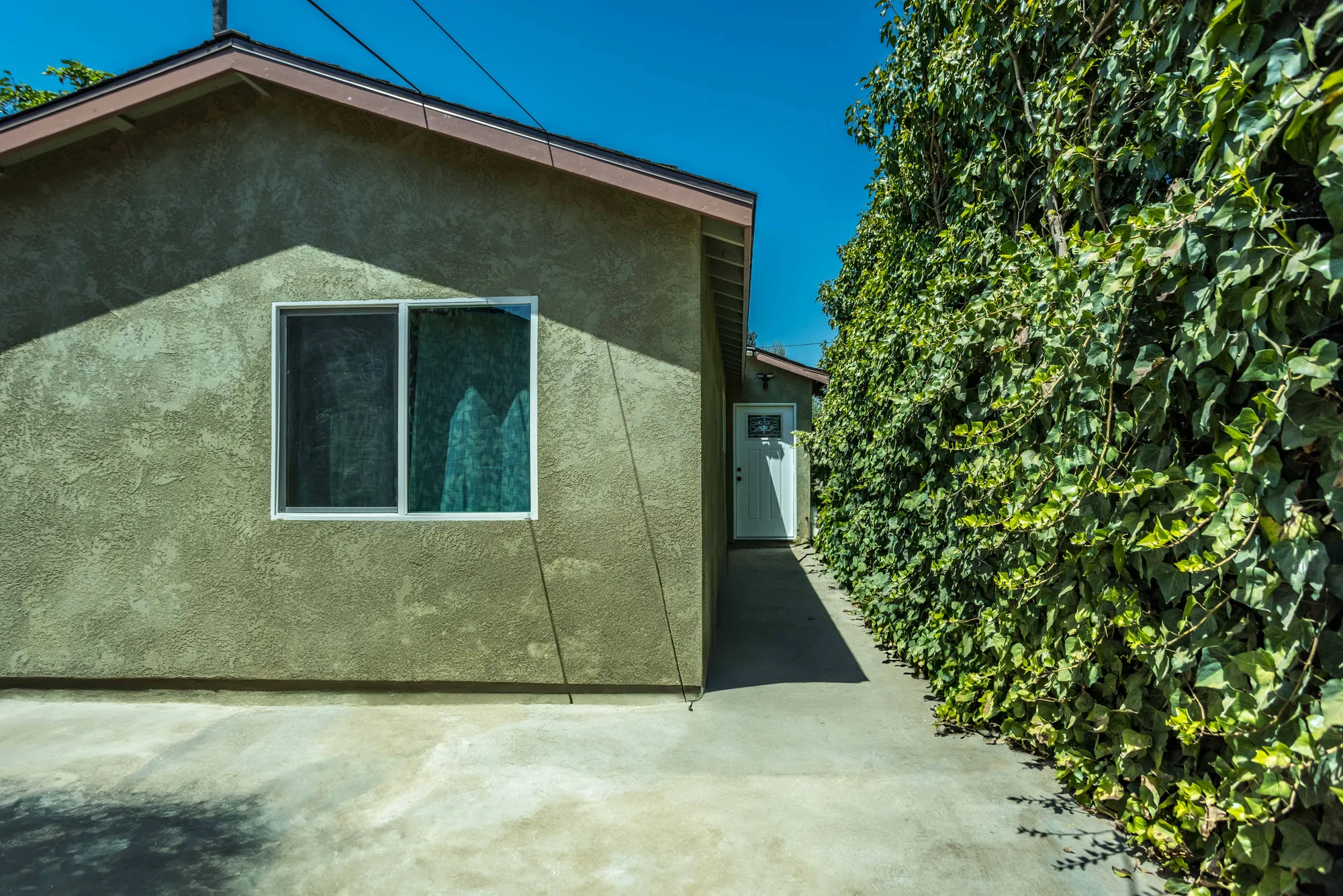 Approach to the addition showing a new slider window in the stucco wall and the white entry door beyond.