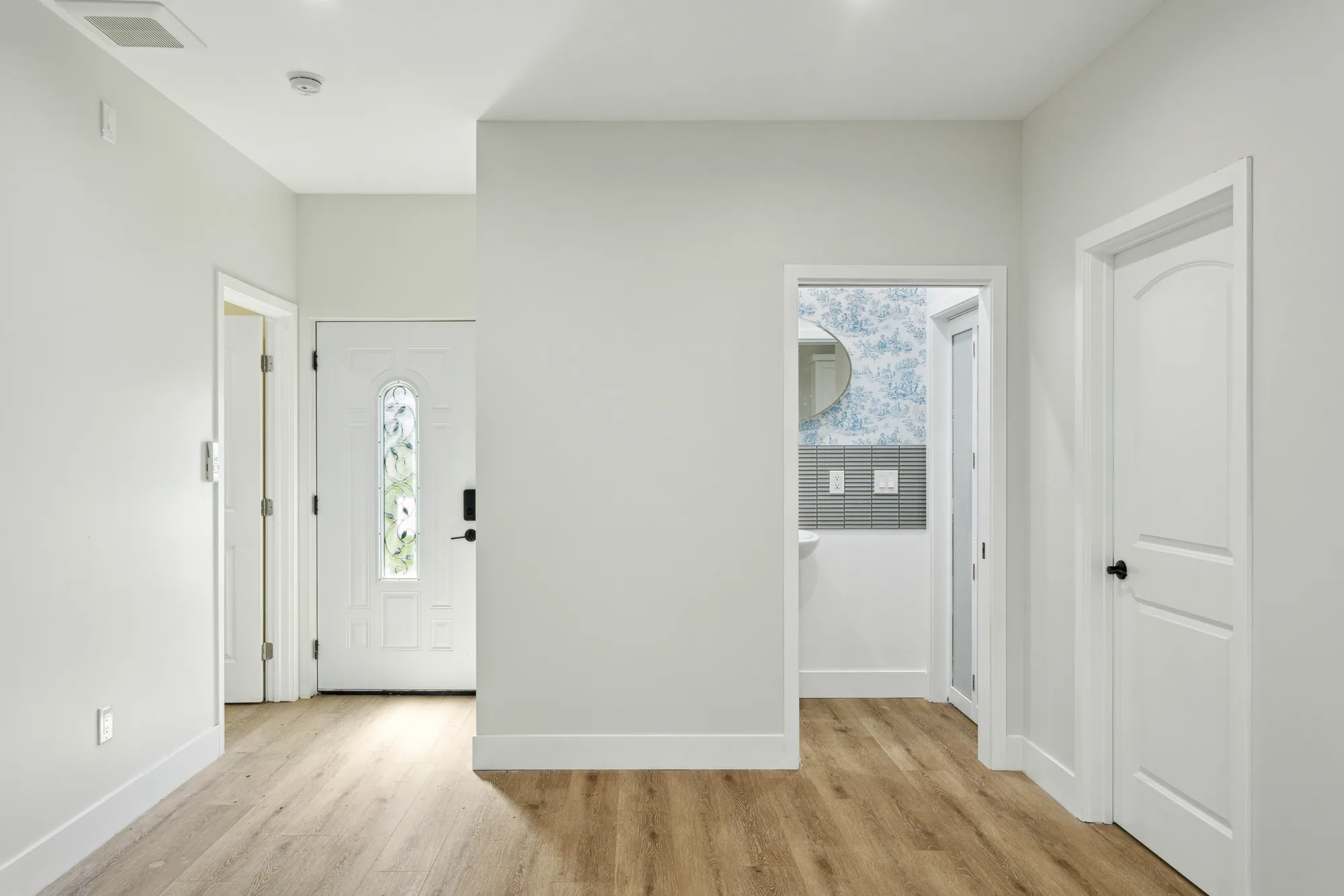 Bright entry hall with a glass-panel front door and an open doorway into a wallpapered powder room.