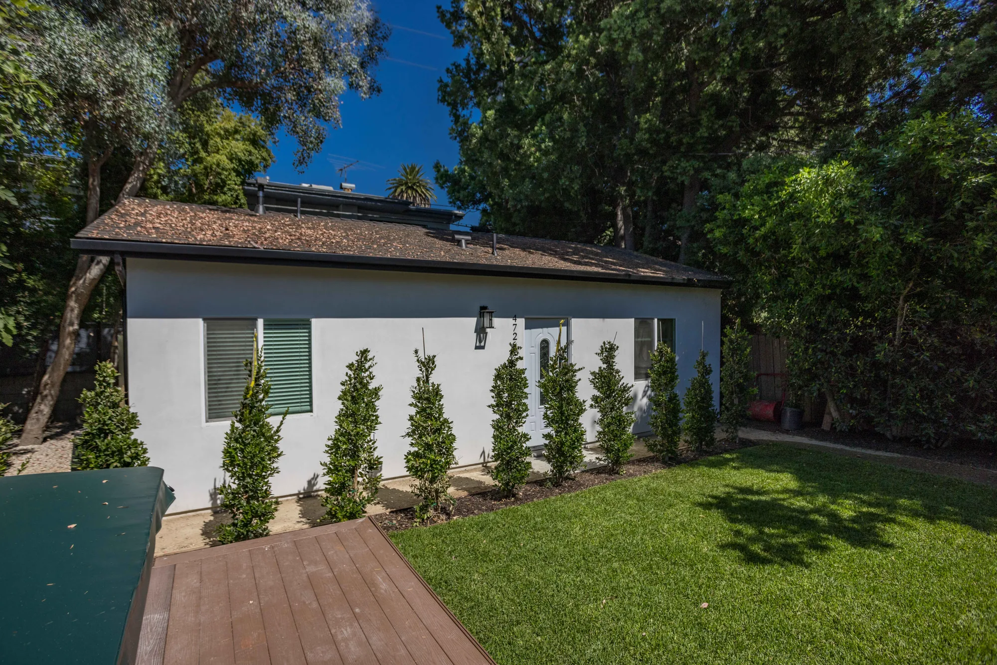 Angled exterior view of the white stucco unit with a wood deck, lawn and new shrub planting.