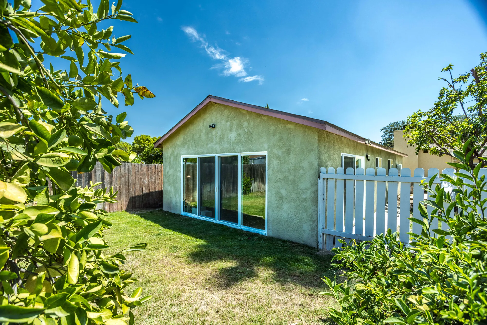 The stucco addition seen through leafy branches, showing its slider, roofline, and side fence.