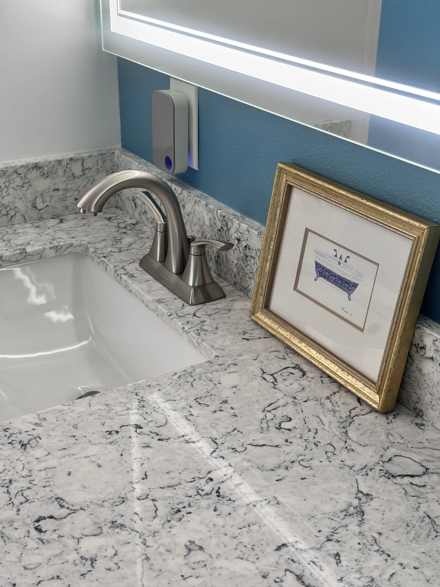 Close view of a brushed nickel faucet and undermount sink set in a heavily veined stone-look counter.