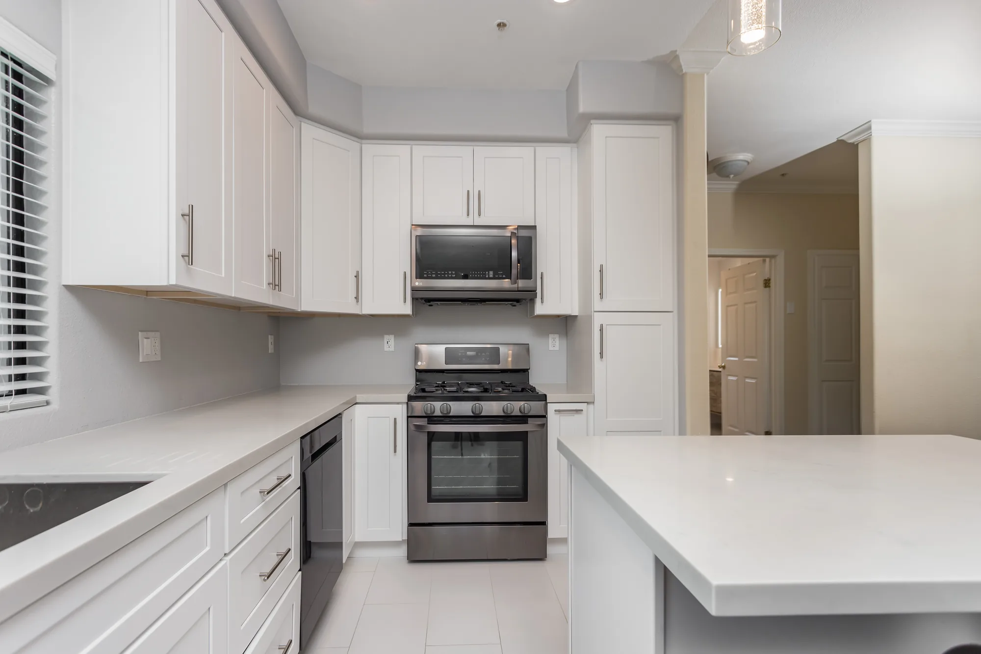 Completed kitchen range wall with white cabinets, tall pantry, stainless range, and light countertops.