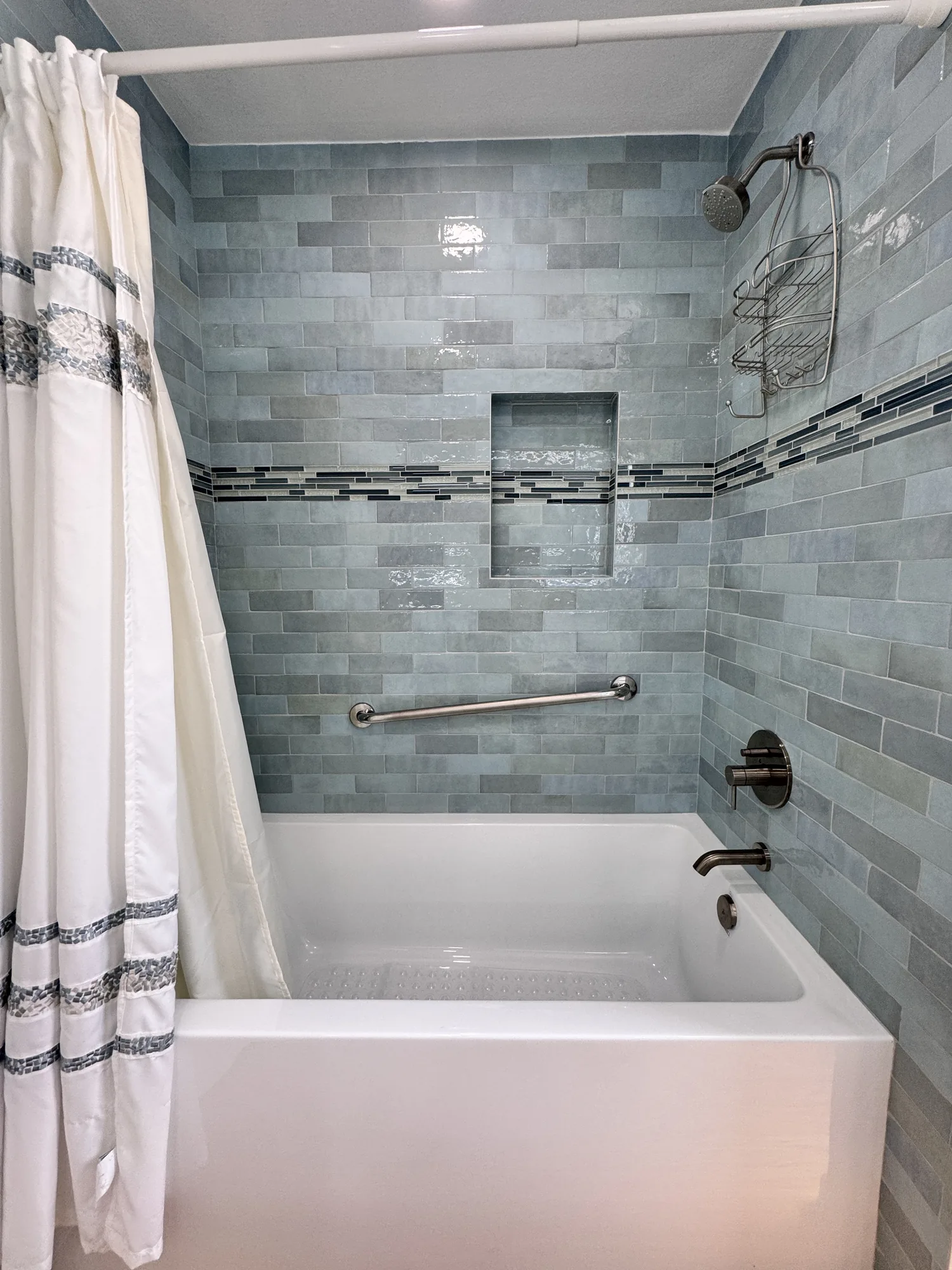 Finished tub and shower with blue-green glazed tile, recessed niche, grab bar and white curtain.