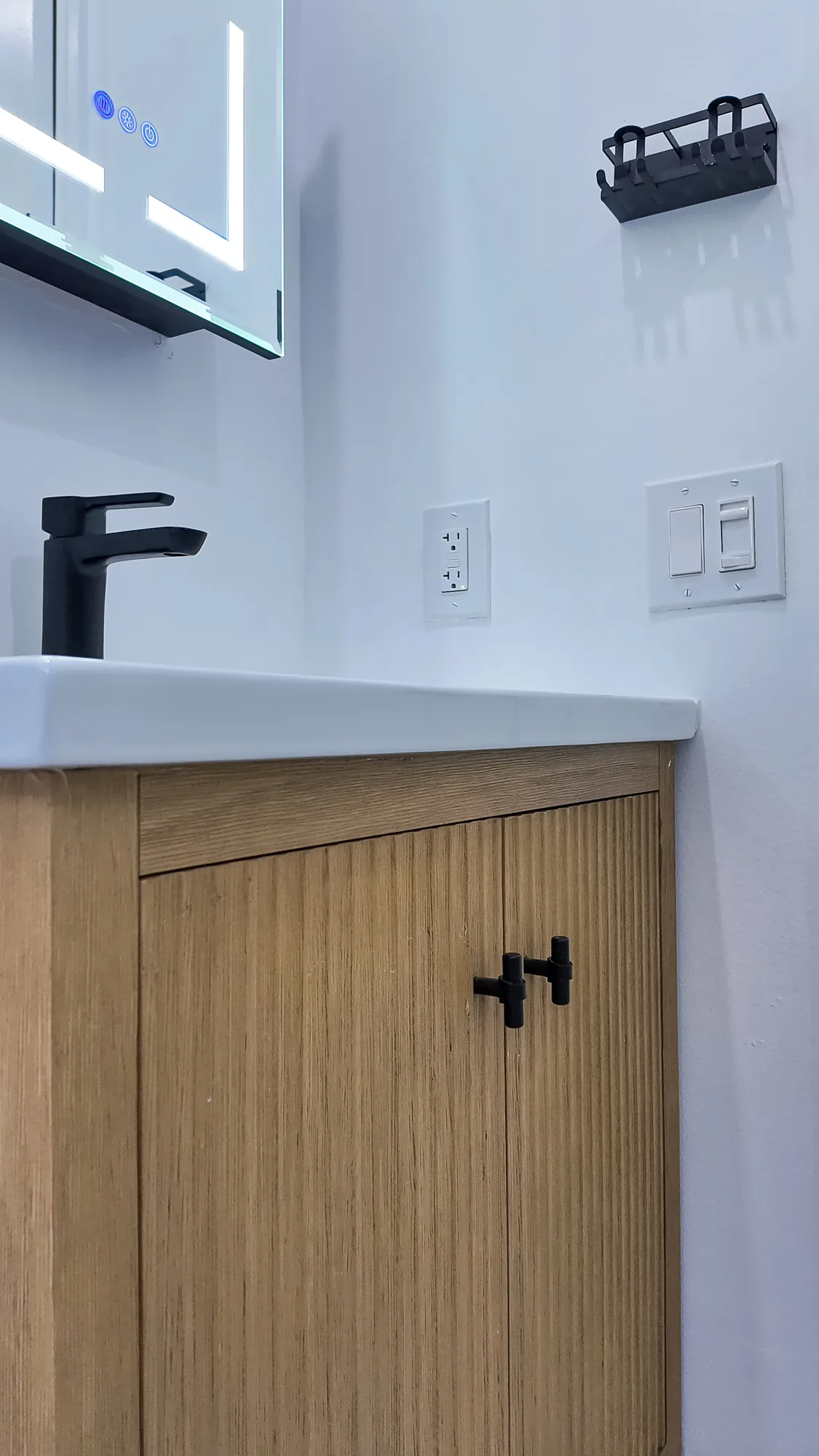 Detail of a fluted wood vanity door with a matte black T-bar knob below a white countertop edge.