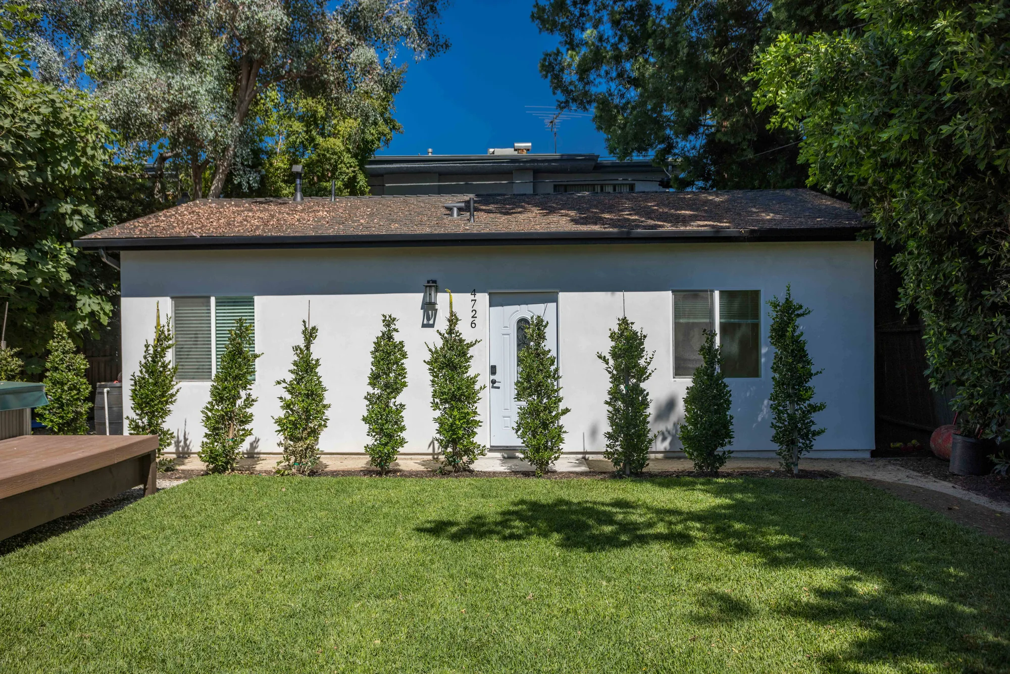Straight-on view of a white stucco unit with a centered entry door and a row of new shrubs.