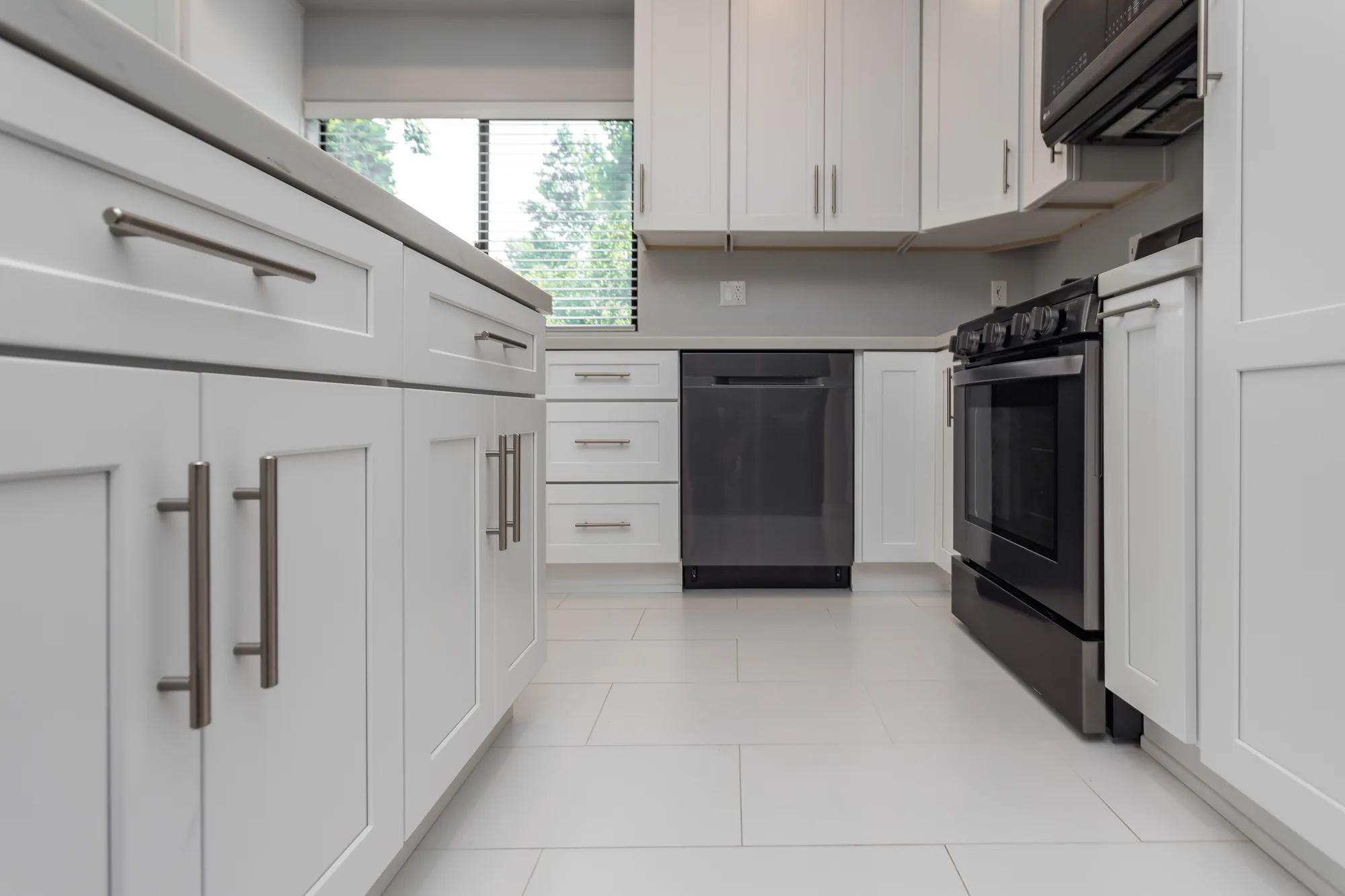 Low view down a white kitchen galley showing base cabinets, a dishwasher, gas range, and tile floor.