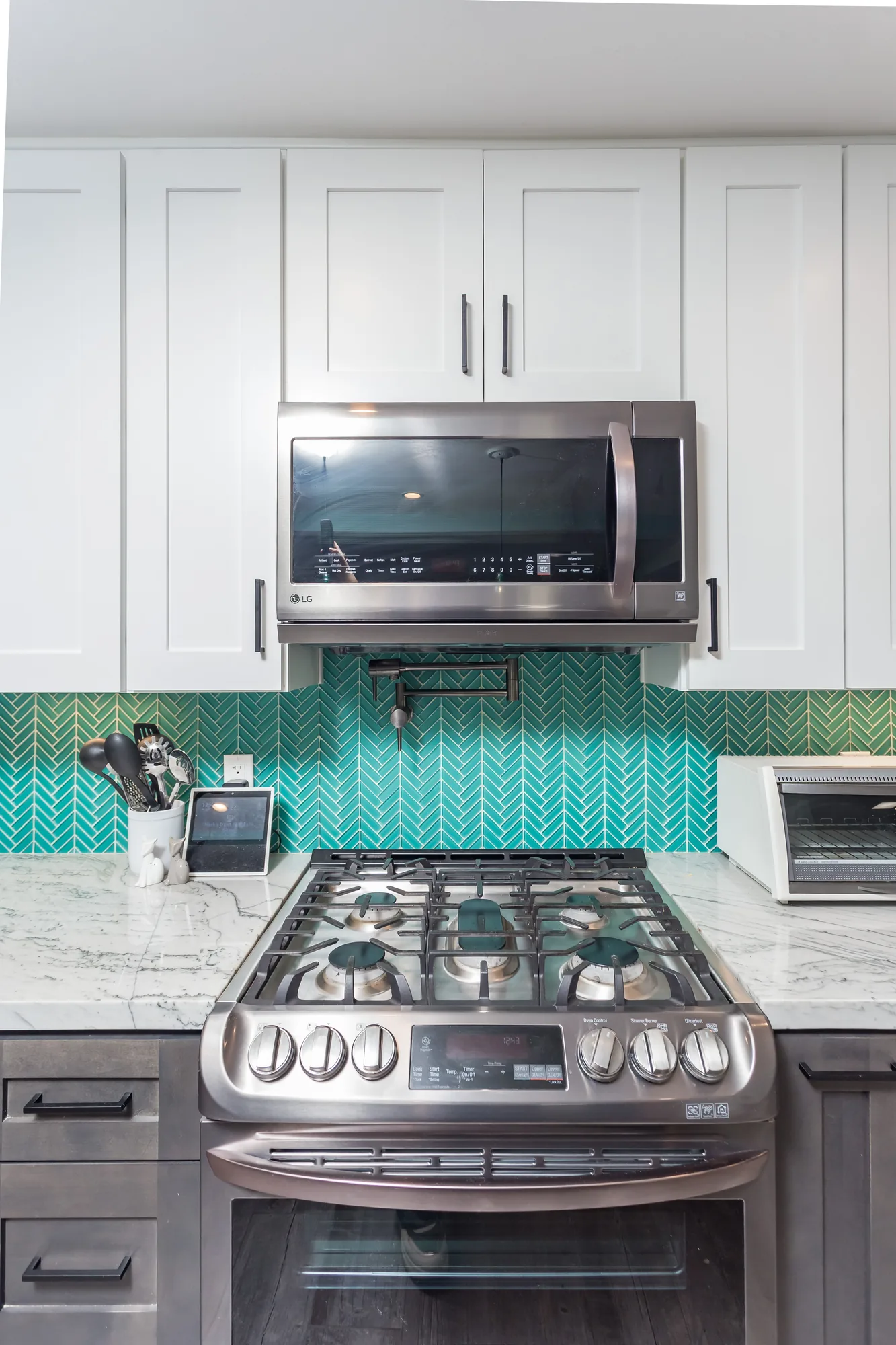 Stainless gas range and over-range microwave set into teal herringbone tile with a pot filler.
