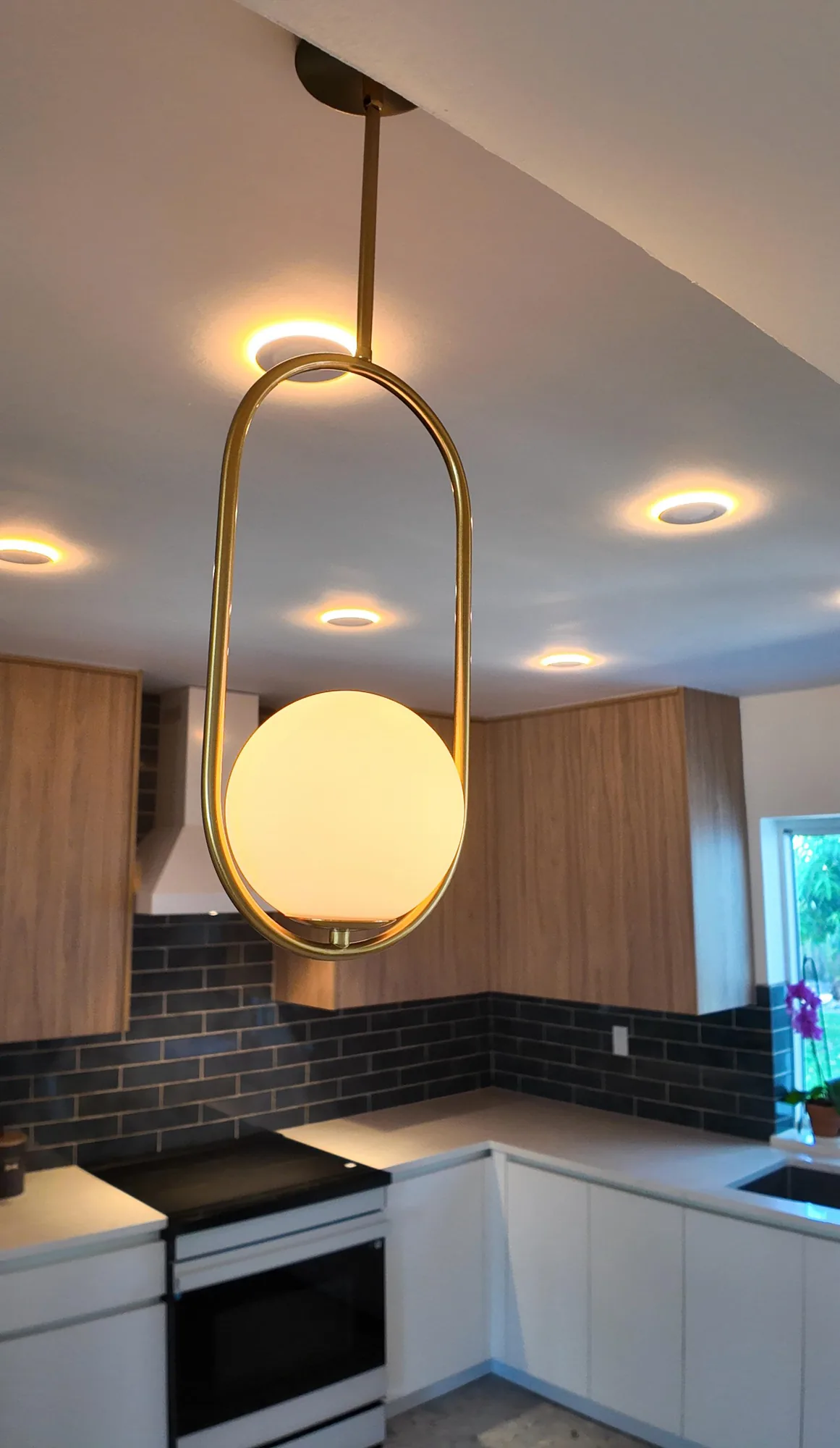 Close view of a brass oval pendant holding an opal glass globe, lit above a kitchen counter.