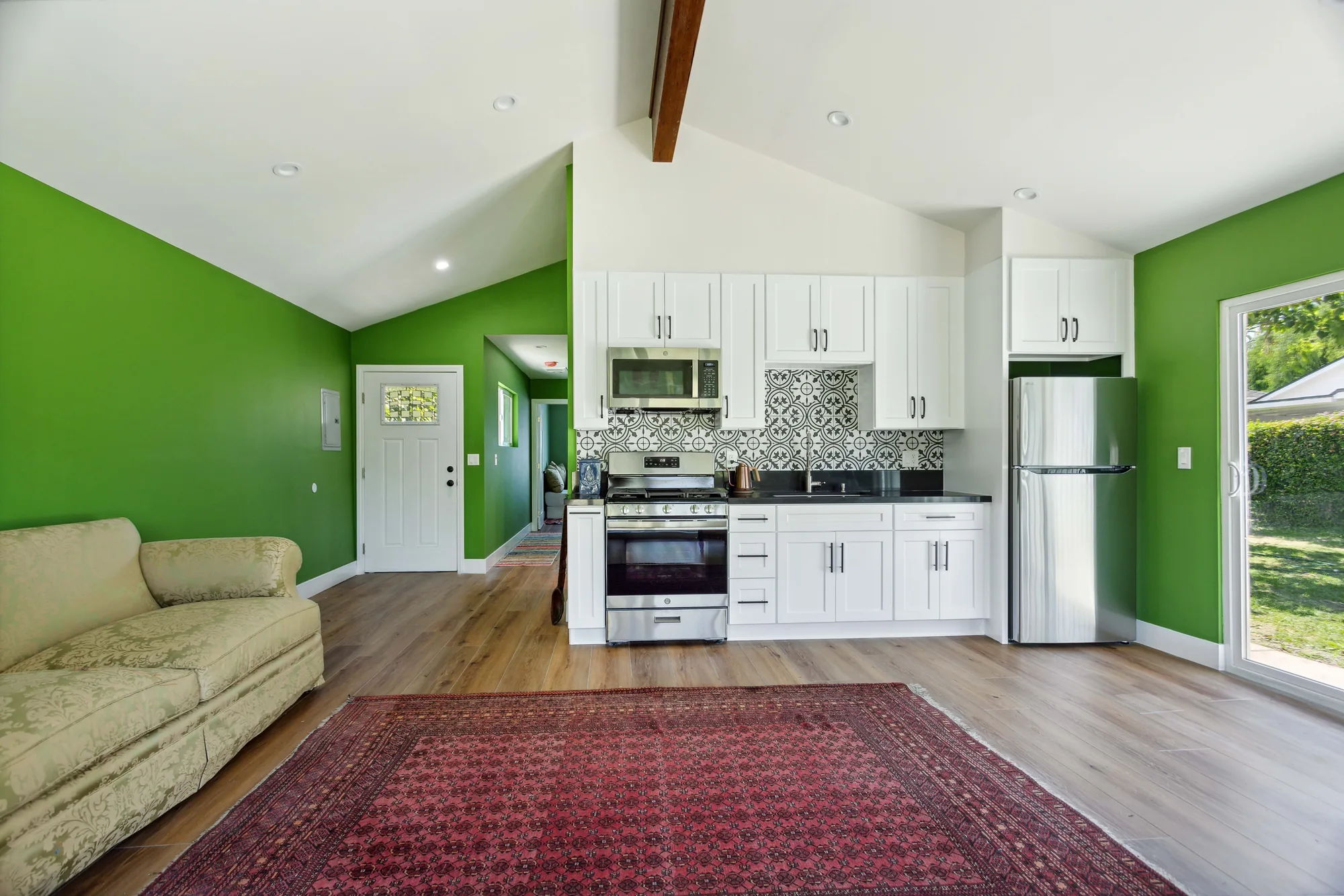 Wide view of a finished great room with sofa, area rug, and white kitchen cabinets under a vaulted ceiling.