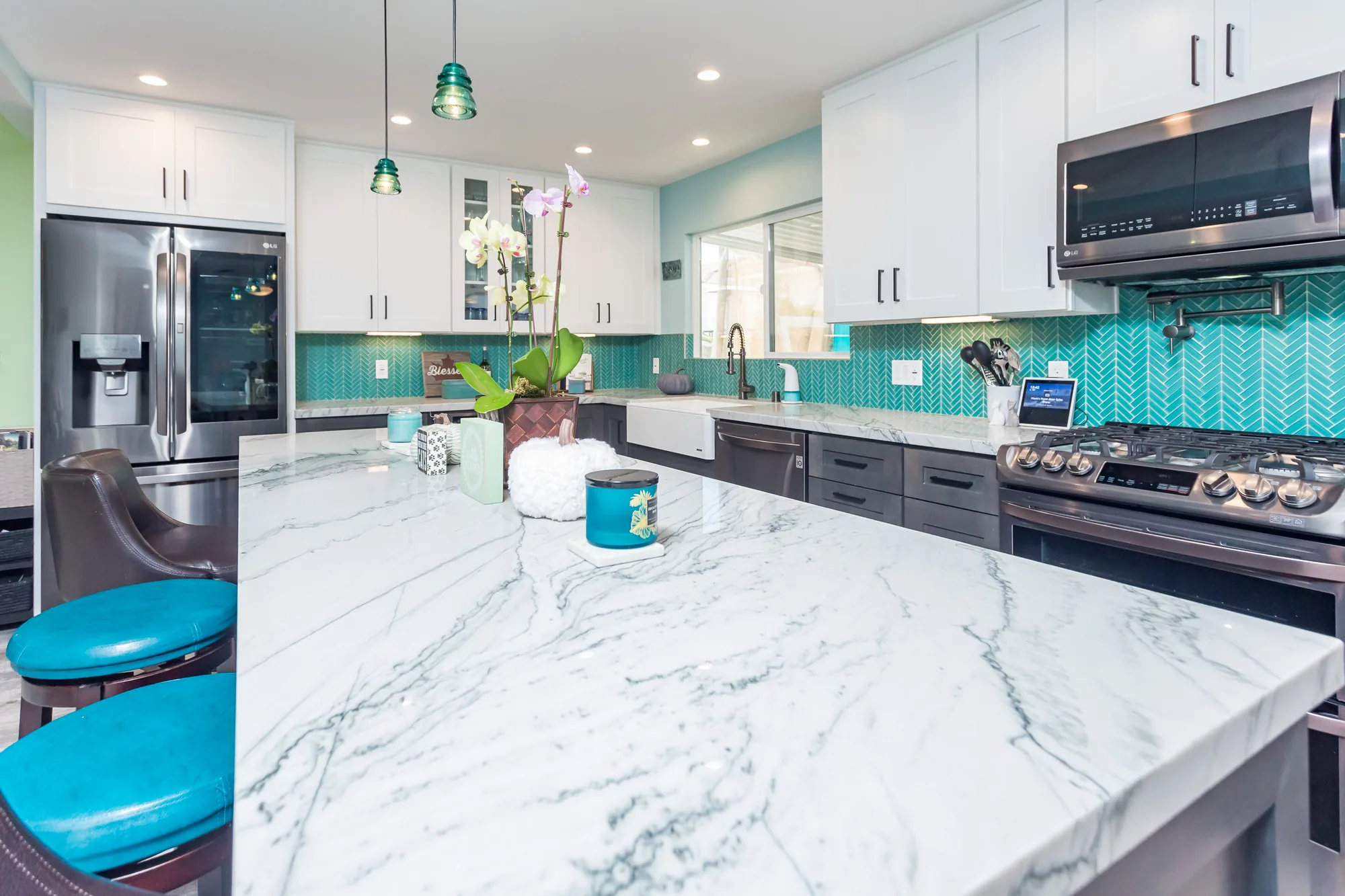 Close view along the island countertop showing heavy gray veining and teal upholstered stools.