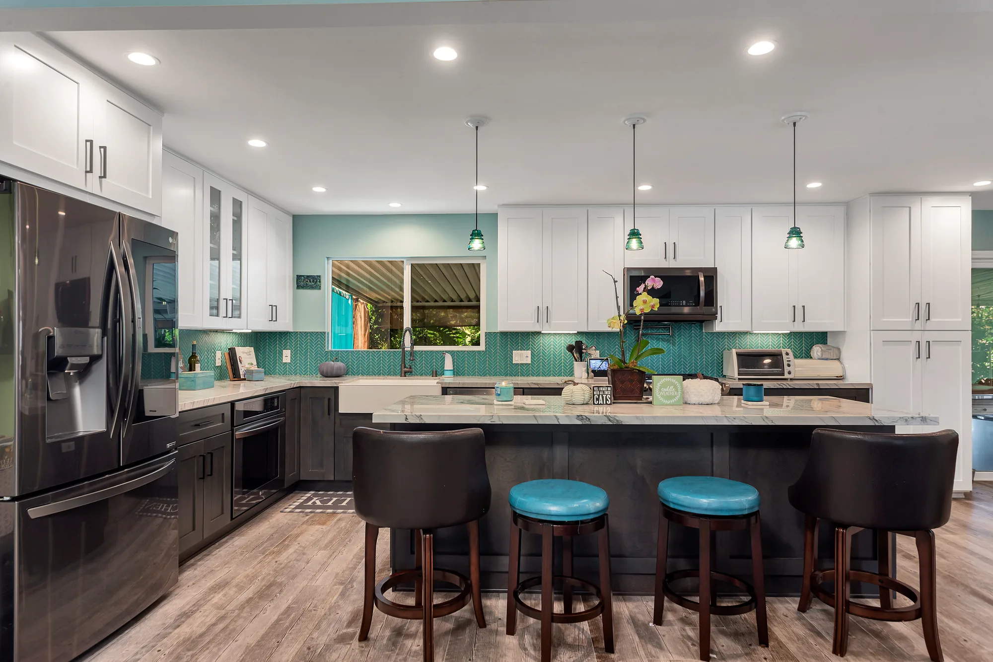 Kitchen island seating with four stools facing white upper cabinets and a teal glass tile backsplash.