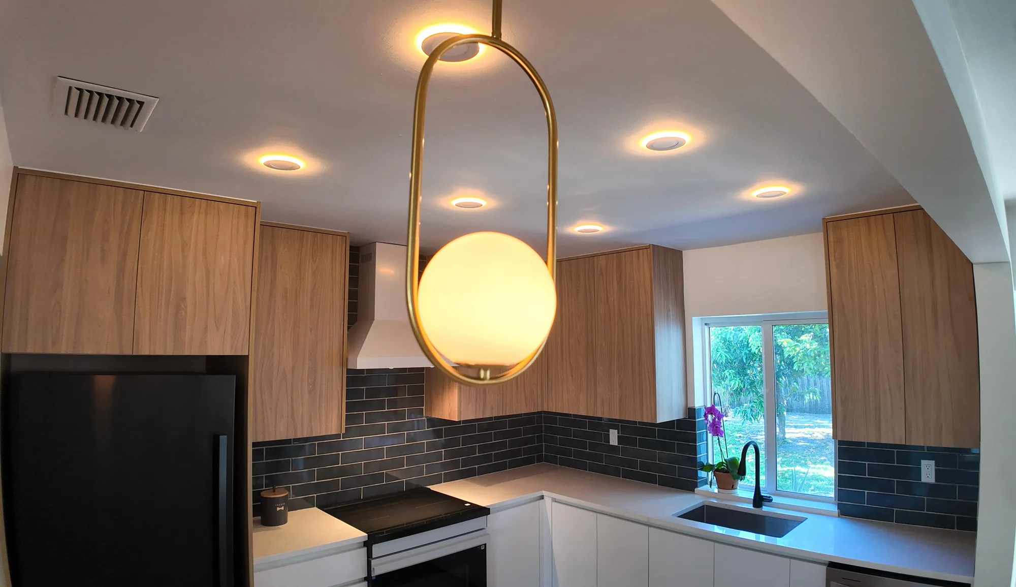 Upward view of a kitchen ceiling with recessed lights and a brass ring pendant holding a glass globe.