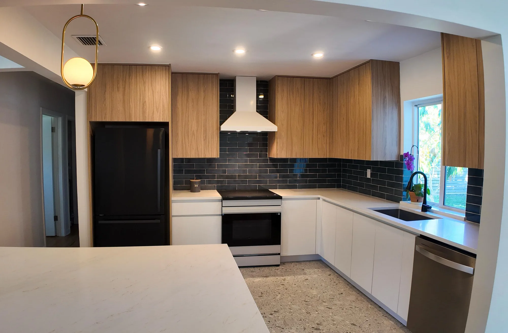 Kitchen viewed from the living area across a light quartz peninsula, with wood cabinets and dark tile.