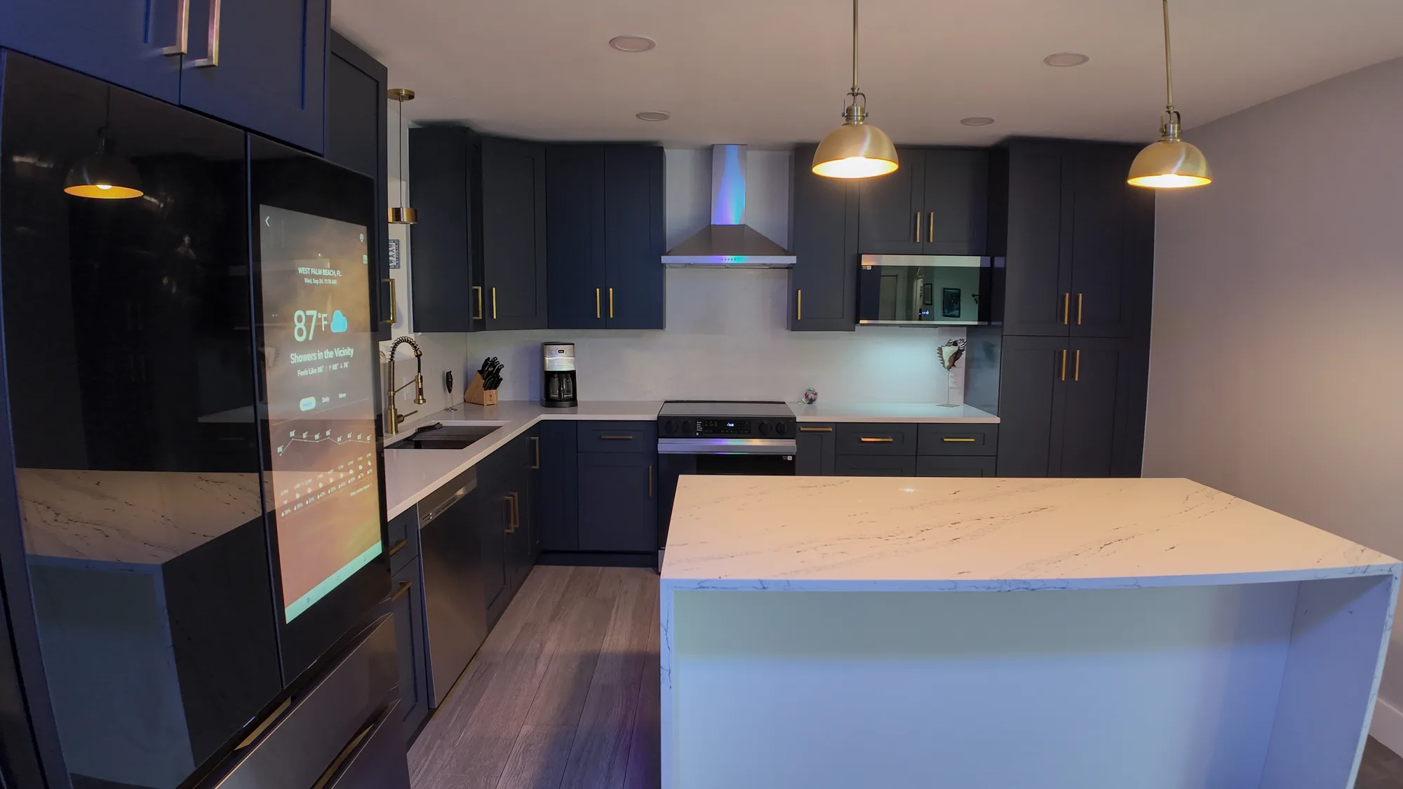 Kitchen seen from the refrigerator corner, showing the quartz island, range wall and navy cabinetry.