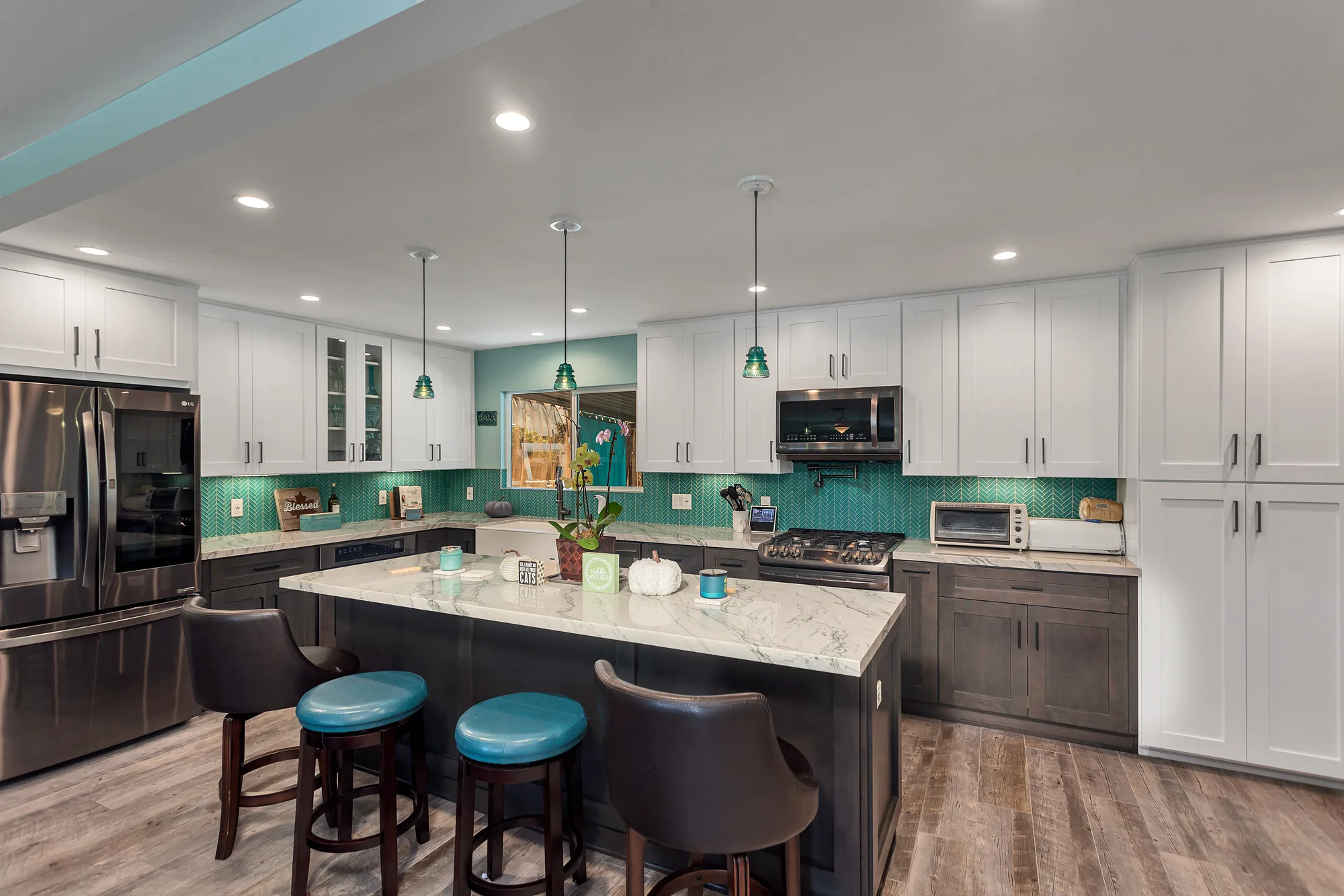 Wide view of a two-tone kitchen with a large stone-topped island and green glass pendant lights.