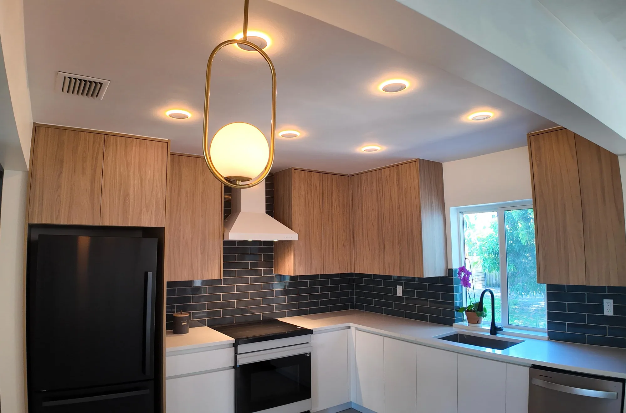 Kitchen photographed toward the ceiling, showing recessed lighting above wood cabinets and dark tile.