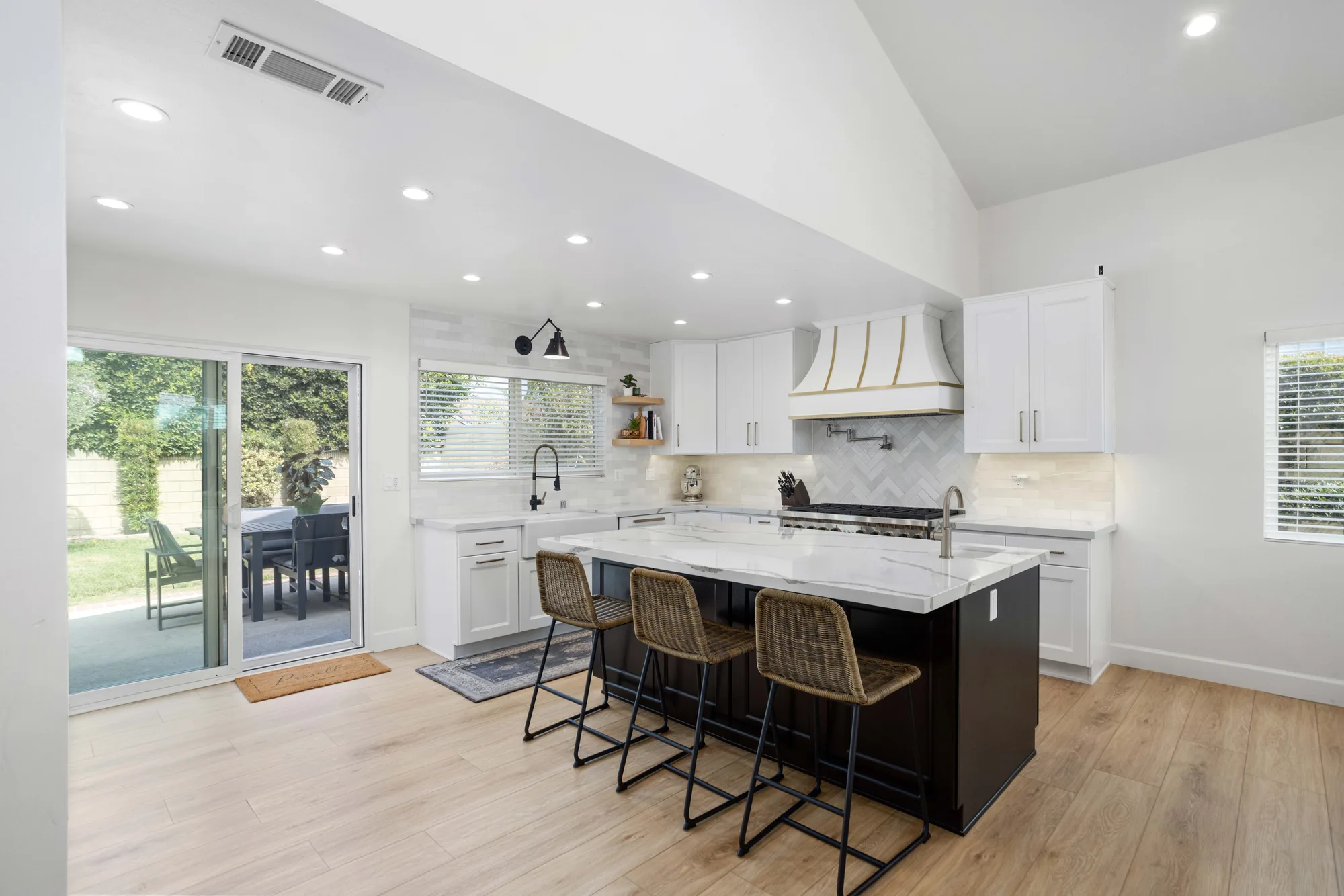 Bright white kitchen with vaulted ceiling, sliding patio doors, brass-strapped hood and a dark island with white marble.