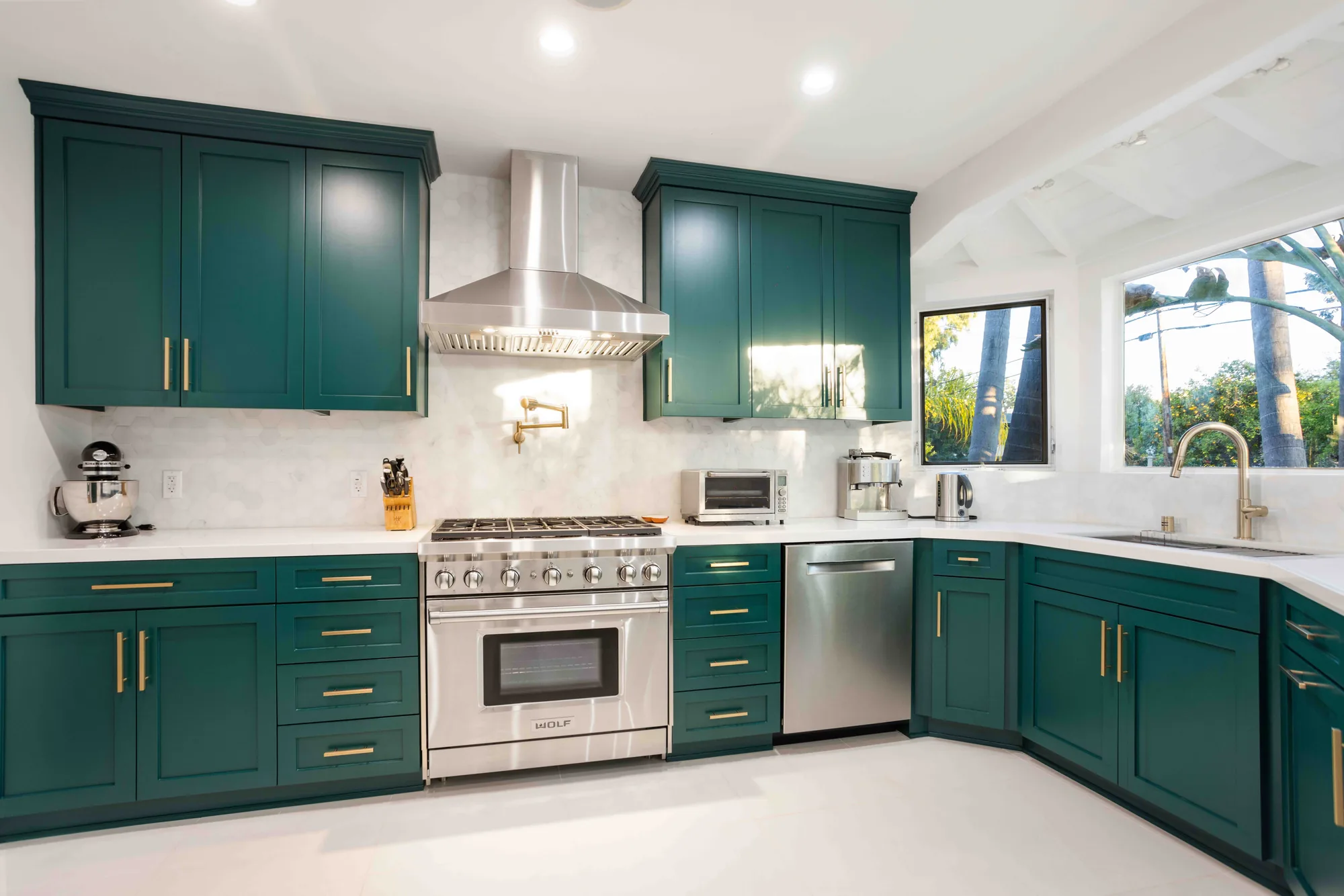 Emerald green kitchen with a stainless Wolf range, marble backsplash and brass hardware.