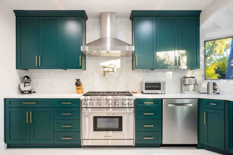 Green shaker kitchen with a stainless Wolf range, vent hood, marble backsplash and brass pulls.