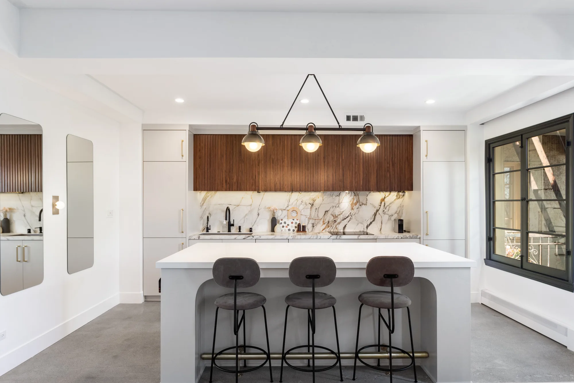 Modern kitchen with a white waterfall island, walnut cabinets and book-matched marble backsplash.