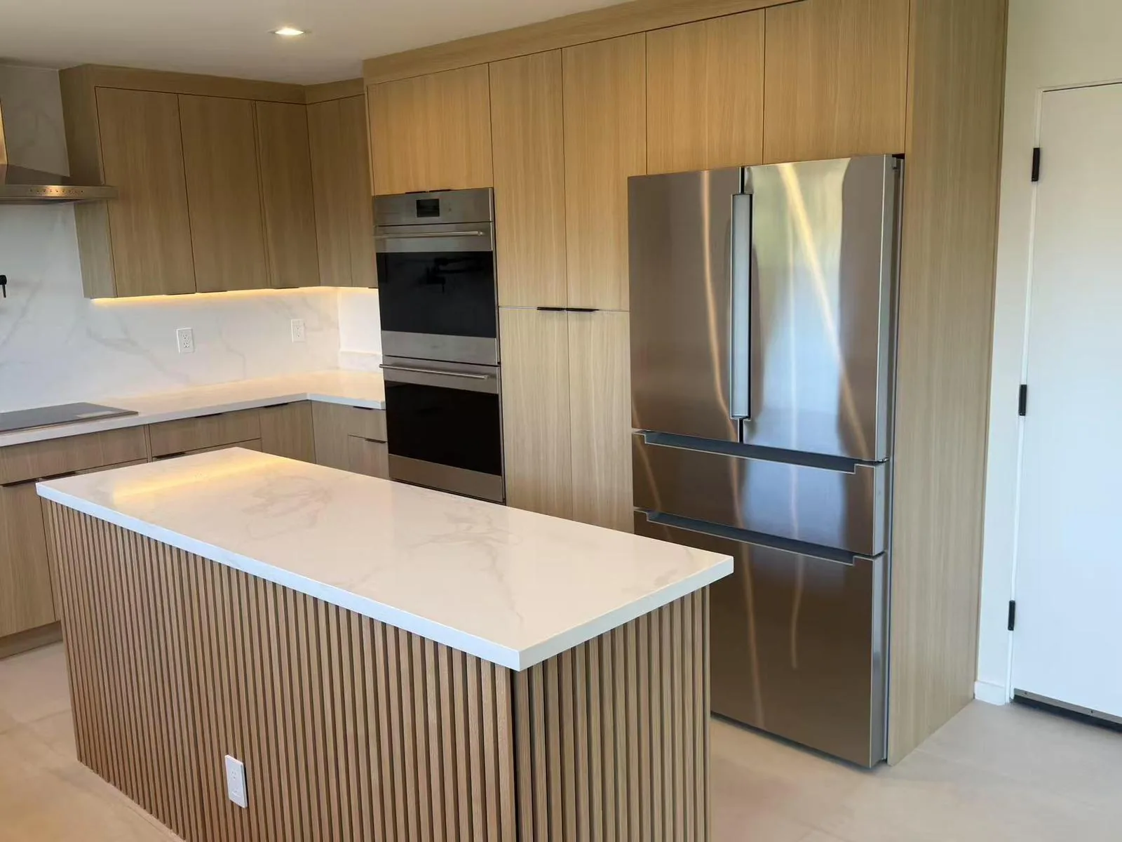 Modern kitchen with light oak cabinets, a fluted waterfall island and stainless steel appliances.