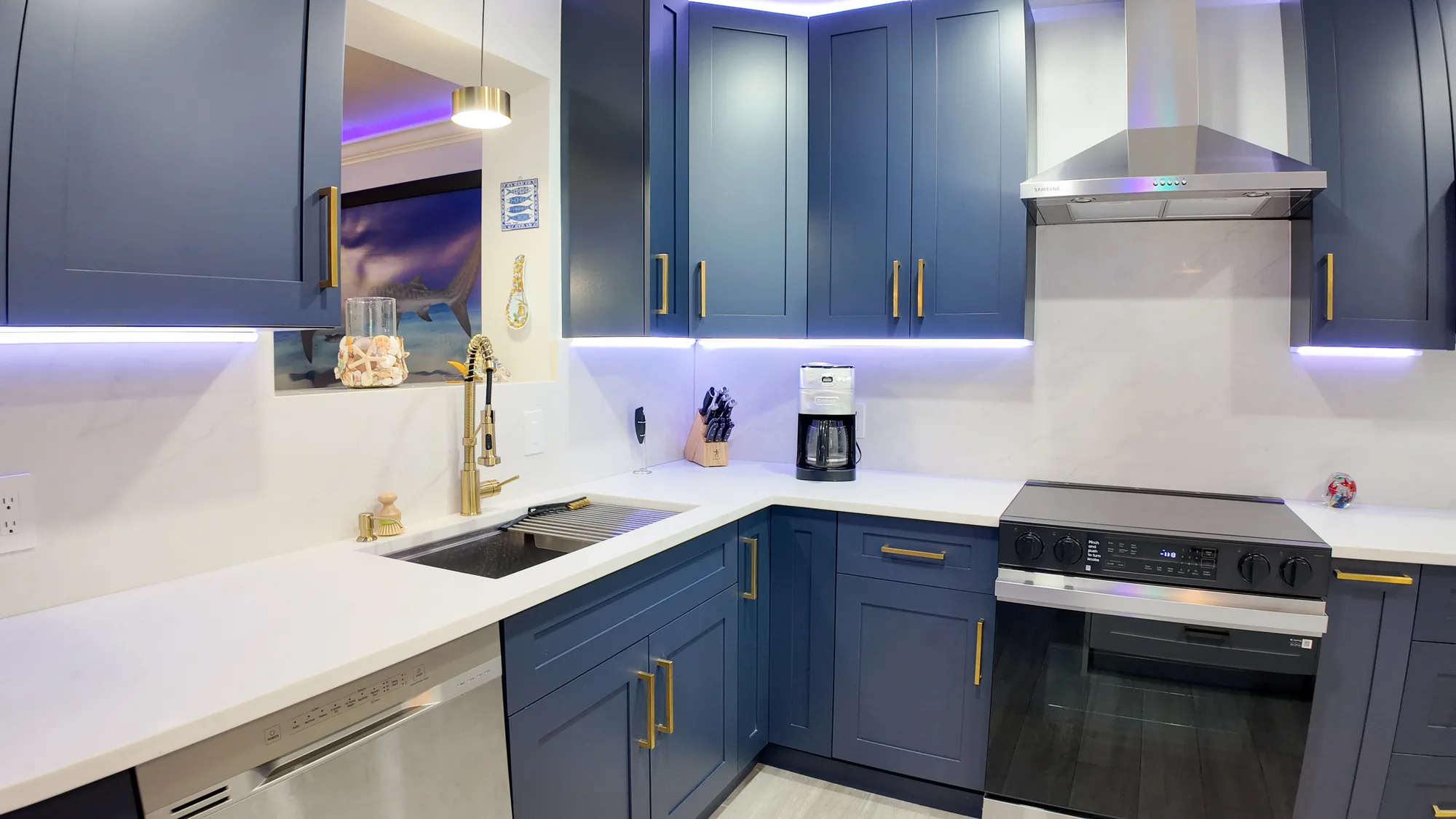 Navy shaker kitchen corner with a gold faucet, quartz counters and a stainless range and hood.